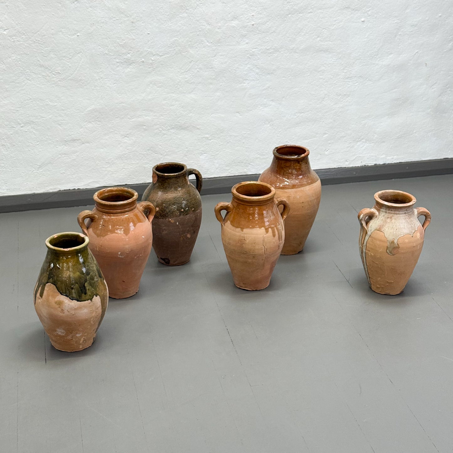 Set of six ceramic vases on a gray floor against a white wall