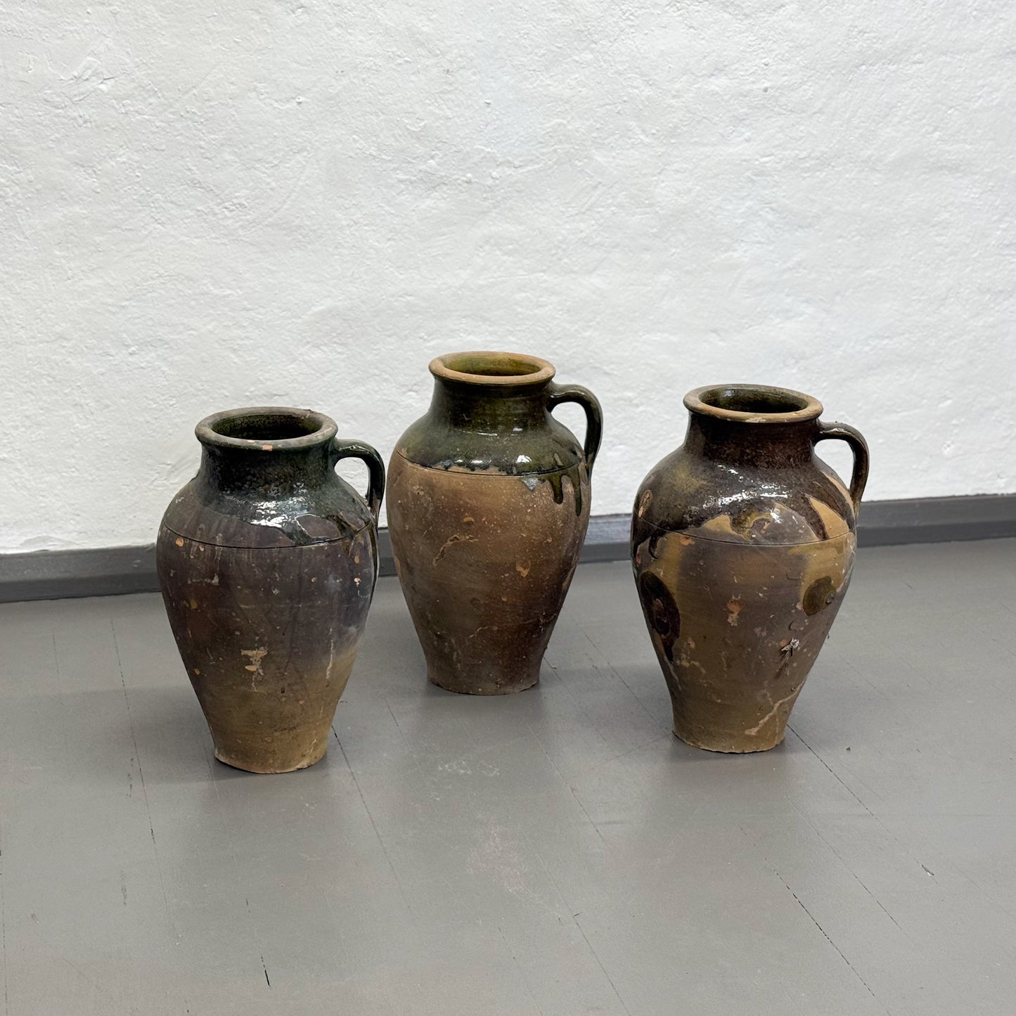 Three vintage ceramic jars with brown and green glaze on a plain floor.