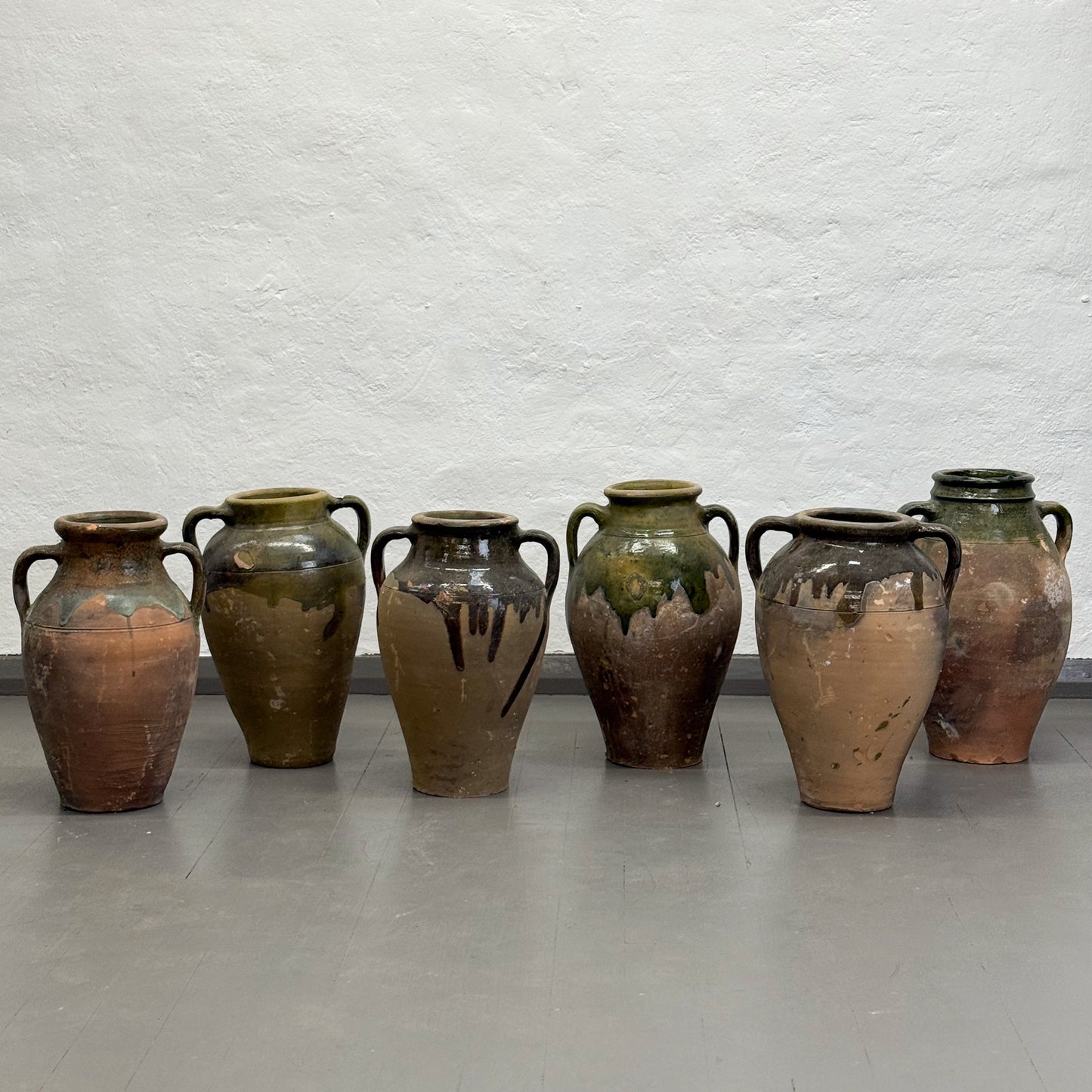 Set of seven ceramic vases with green and brown glaze on a plain background