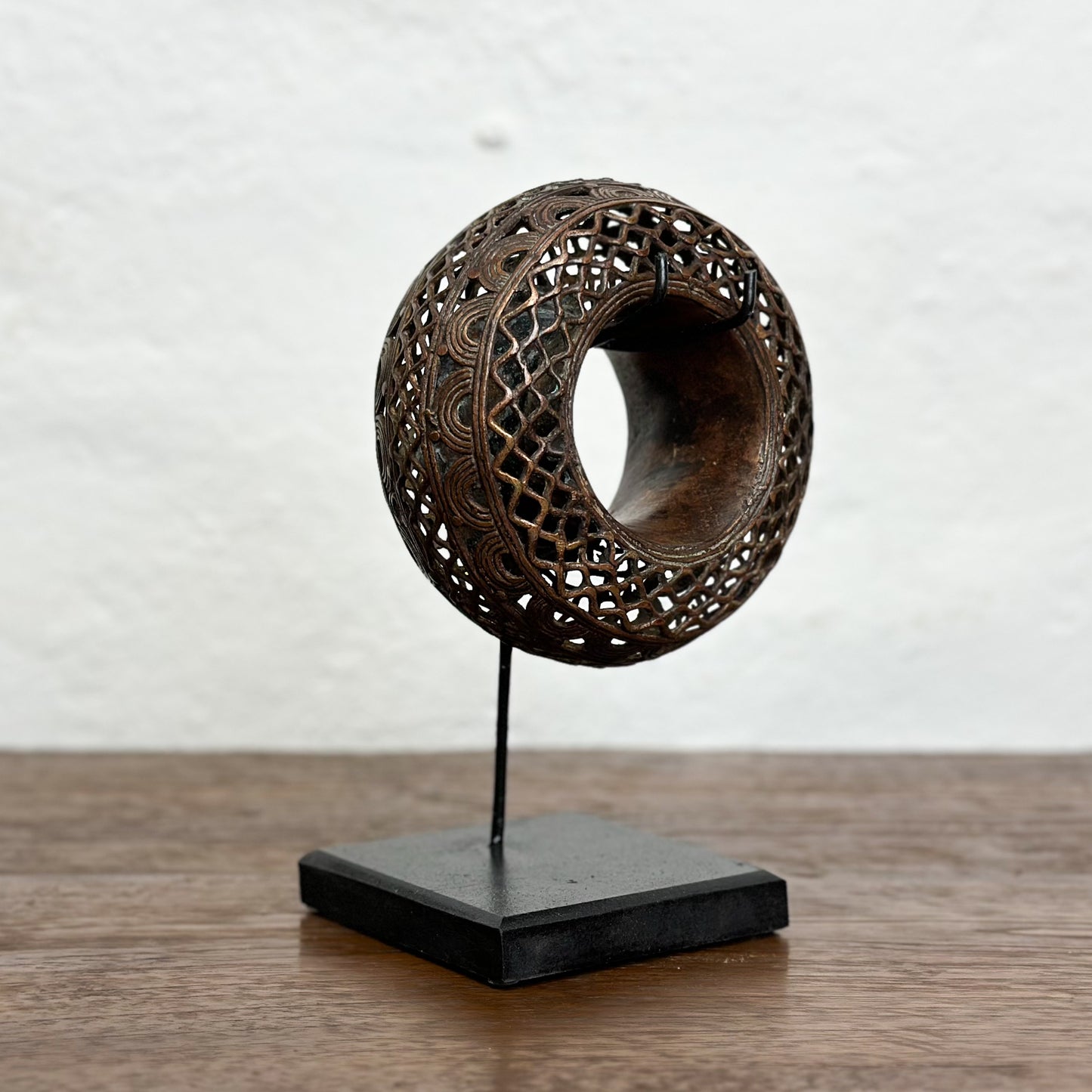 Three bronze anklets with intricate geometric patterns displayed on individual stands against a white background.