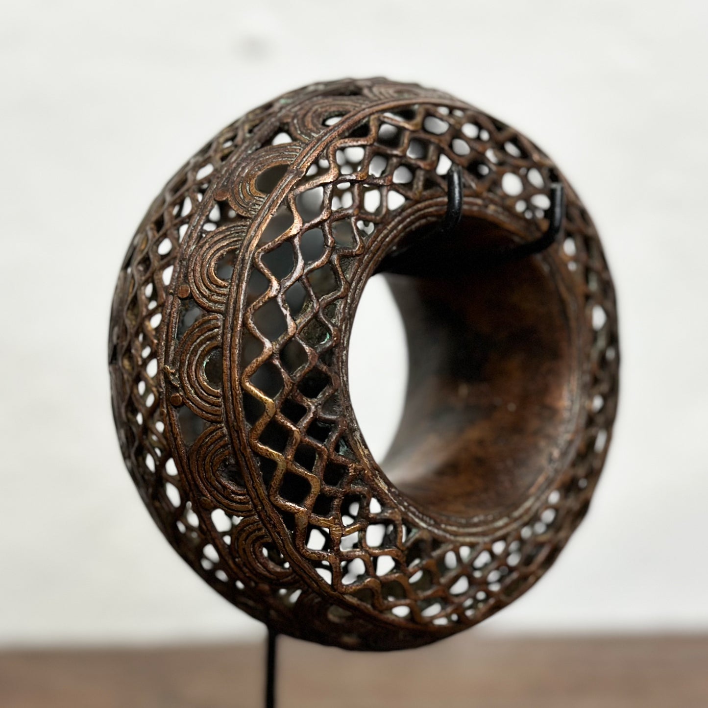Three bronze anklets with intricate geometric patterns displayed on individual stands against a white background.
