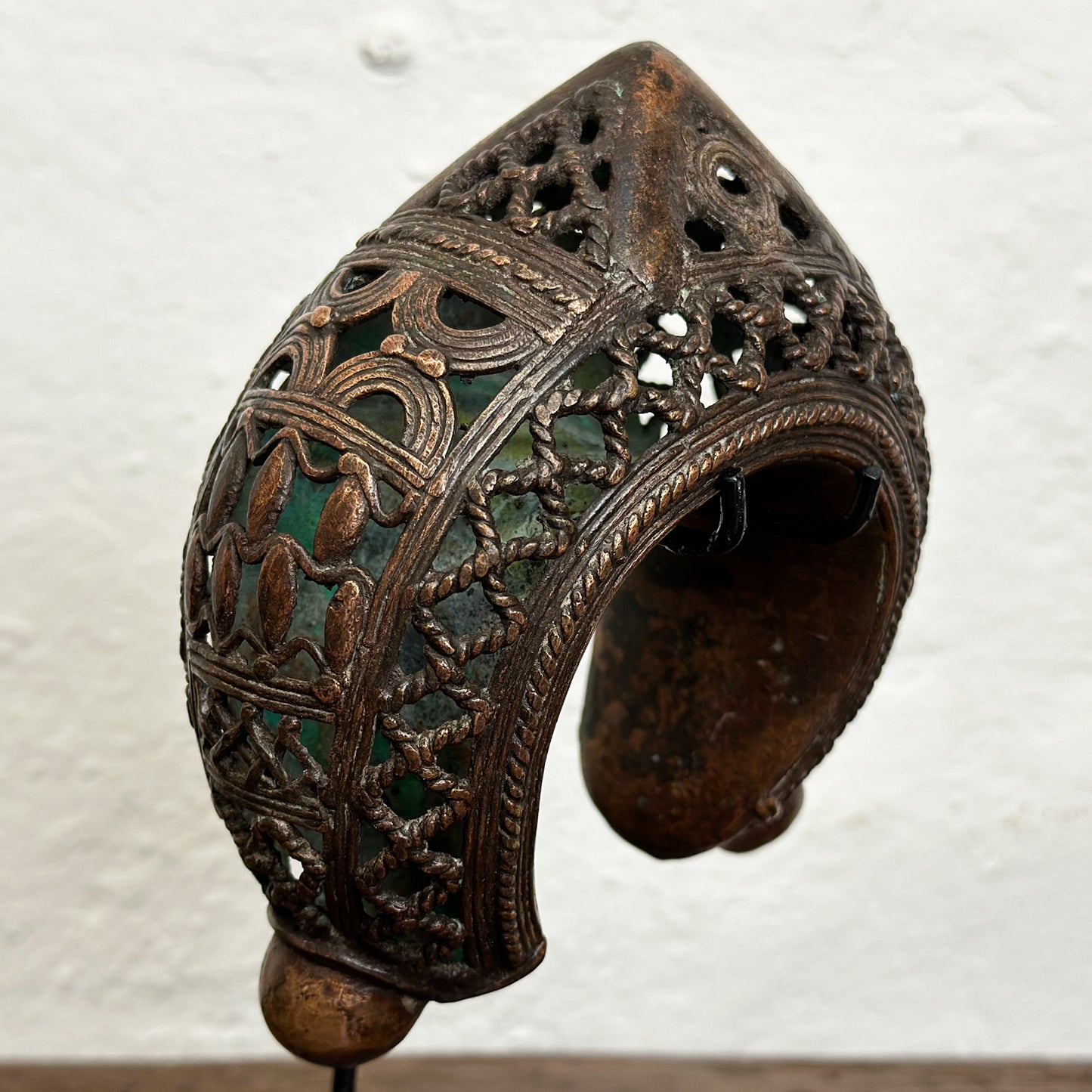 Three bronze anklets with intricate geometric patterns displayed on individual stands against a white background.