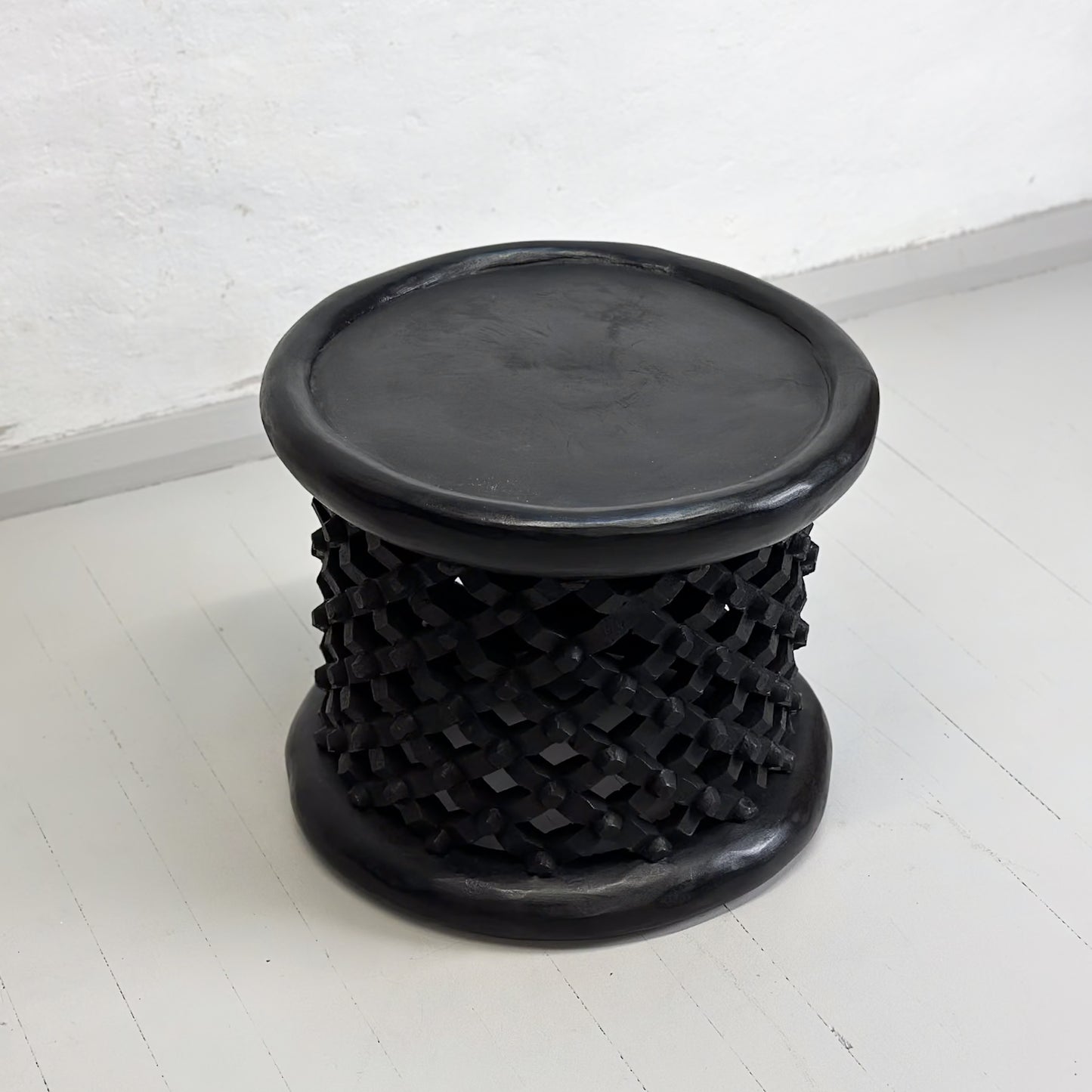 A small Bamileke stool from Cameroon with a geometric pattern, predominantly in black color.