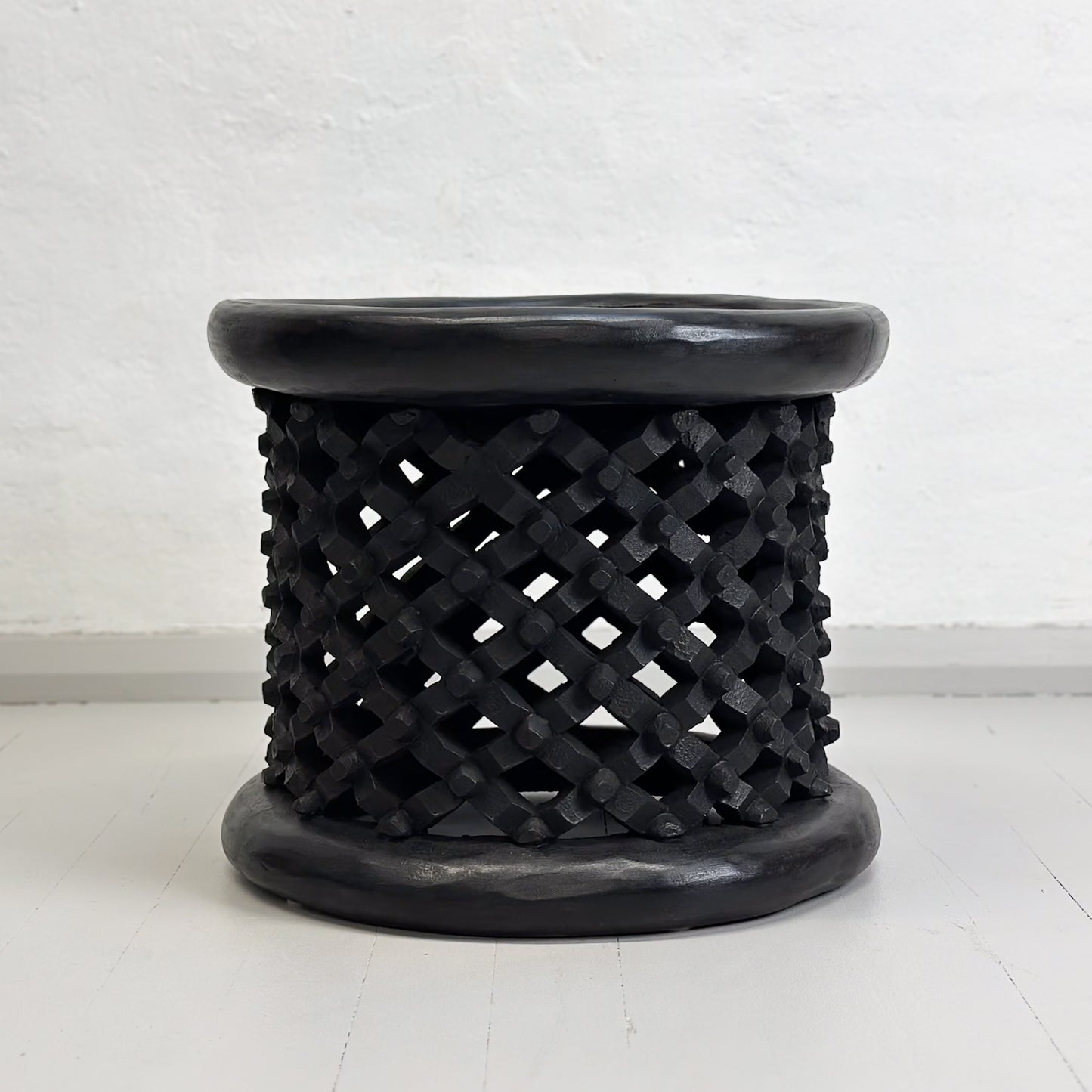 A small Bamileke stool from Cameroon with a geometric pattern, predominantly in black color.