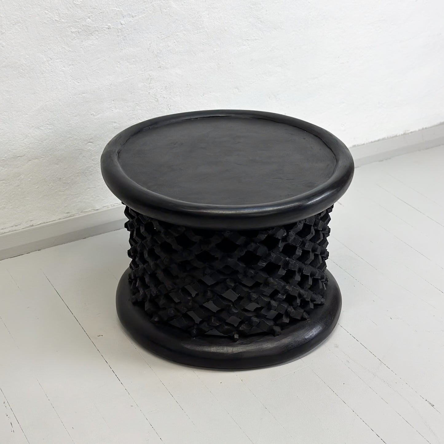 A black Bamileke stool with a geometric pattern, made of wood, against a white background.