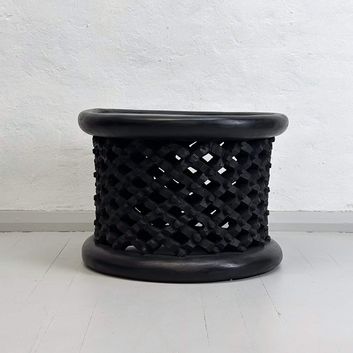 A black Bamileke stool with a geometric pattern, made of wood, against a white background.