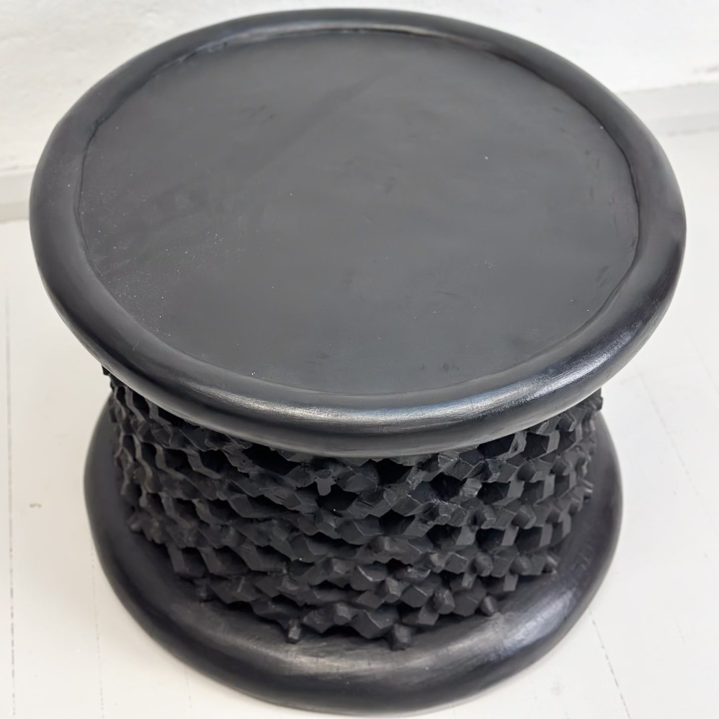 A black Bamileke stool with a geometric pattern, made of wood, against a white background.