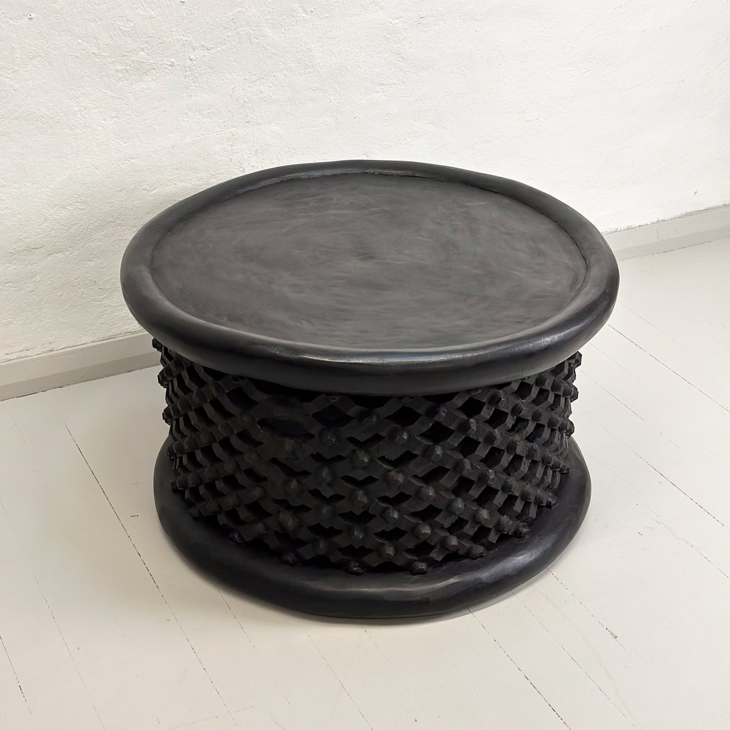 A black Bamileke coffee table with a geometric pattern, likely made of wood, against a white background.