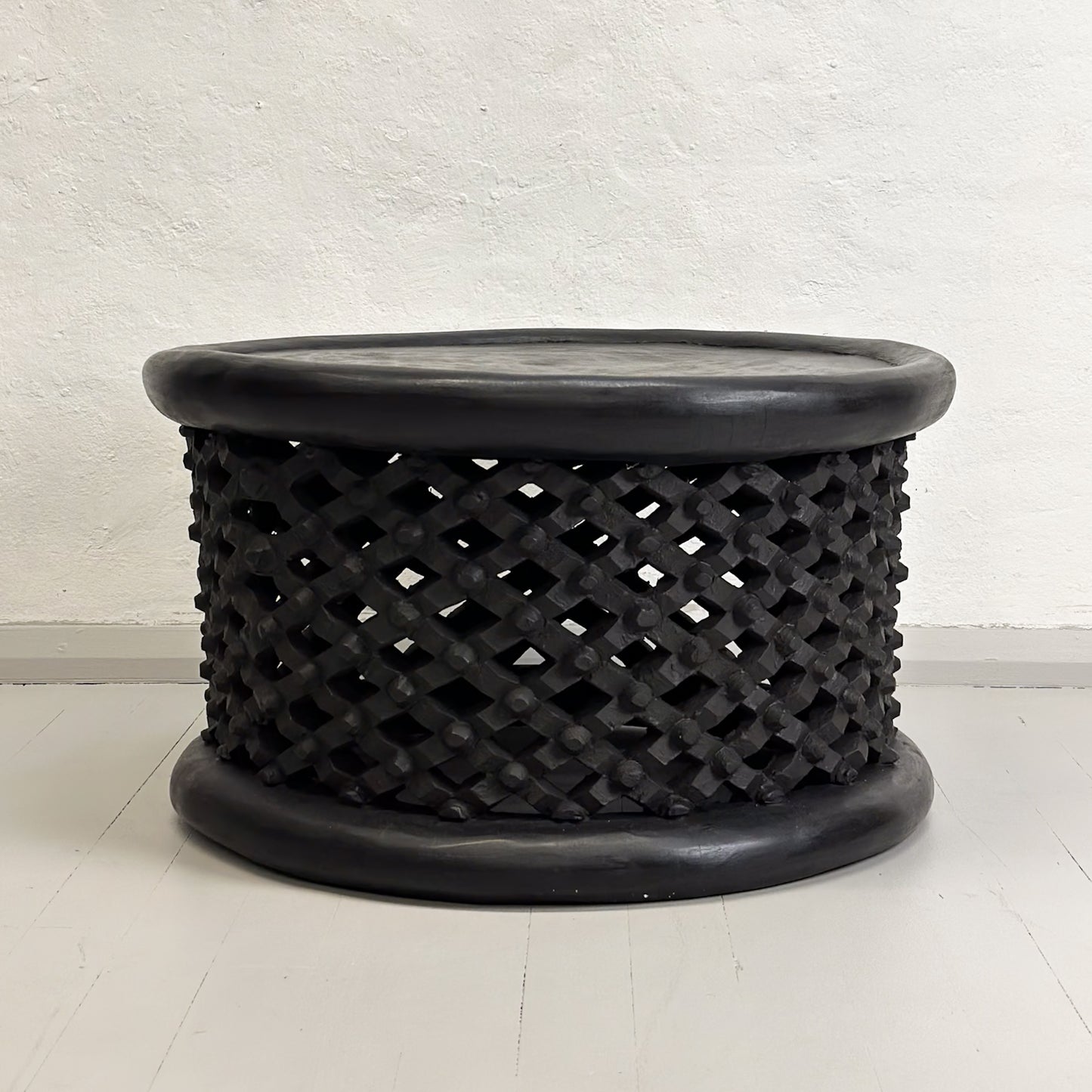 A black Bamileke coffee table with a geometric pattern, likely made of wood, against a white background.