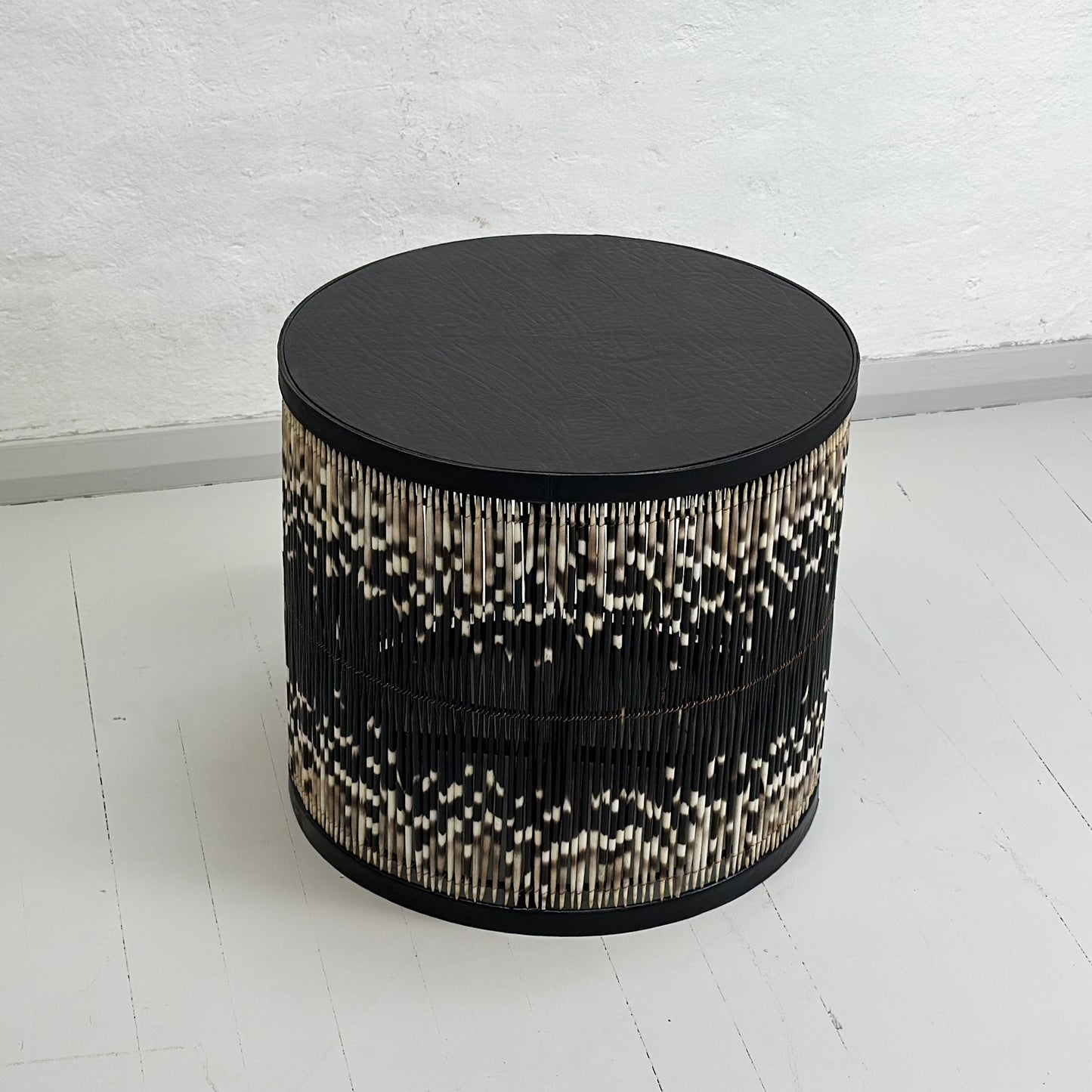 A round porcupine quill table with black and white quills, placed on a neutral background.