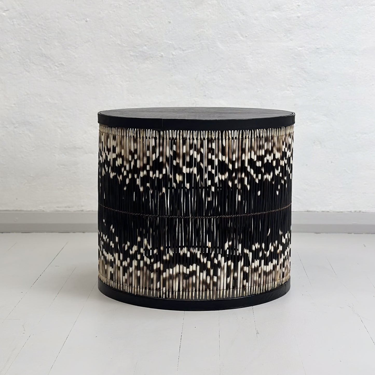 A round porcupine quill table with black and white quills, placed on a neutral background.