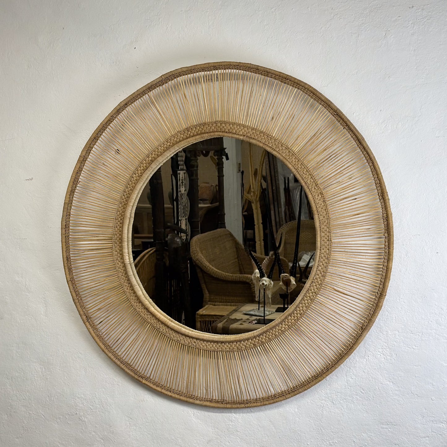 A round mirror with a natural beige straw frame, hanging on a wall.