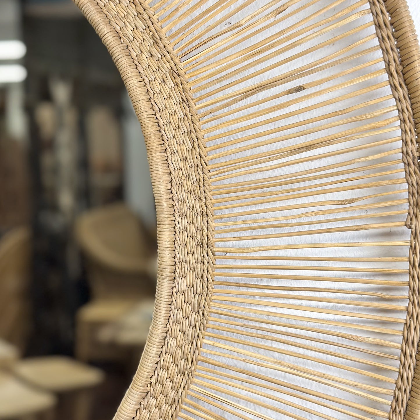 A round mirror with a natural beige straw frame, hanging on a wall.