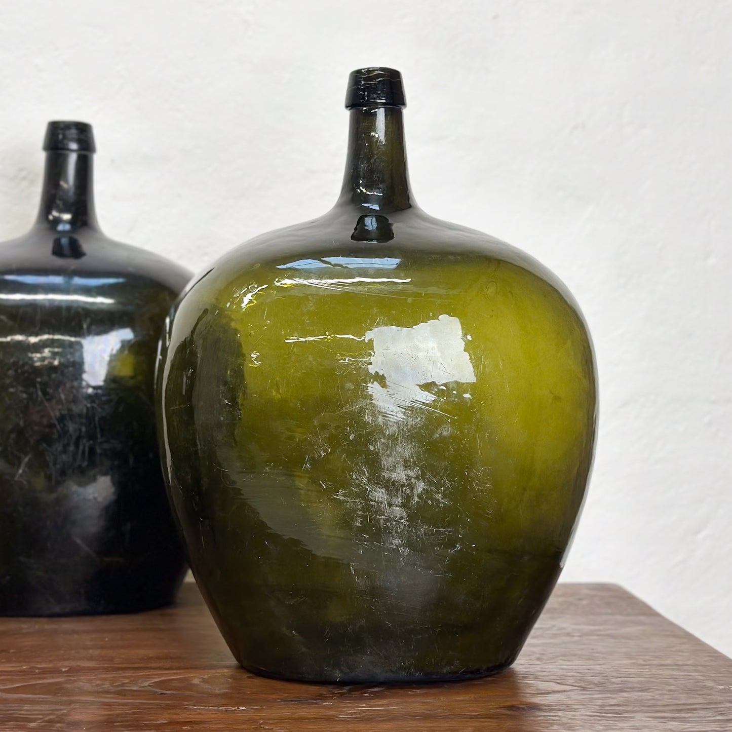 Three oval demijohn glass vases with a dark tint, displayed on a wooden surface against a neutral background.