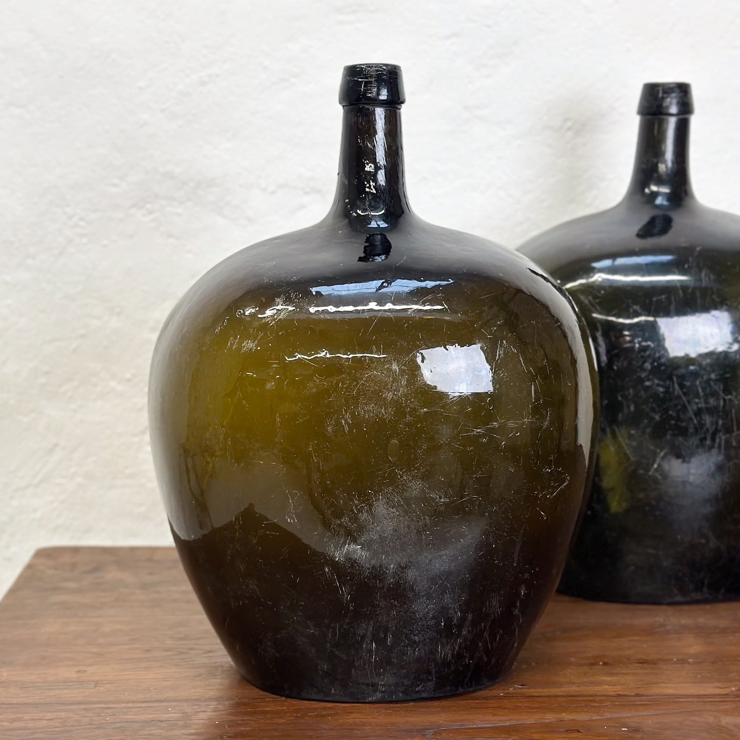 Three oval demijohn glass vases with a dark tint, displayed on a wooden surface against a neutral background.