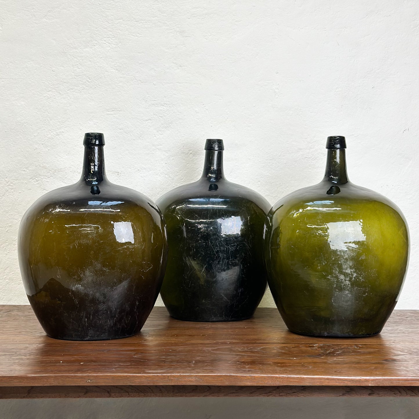 Three oval demijohn glass vases with a dark tint, displayed on a wooden surface against a neutral background.
