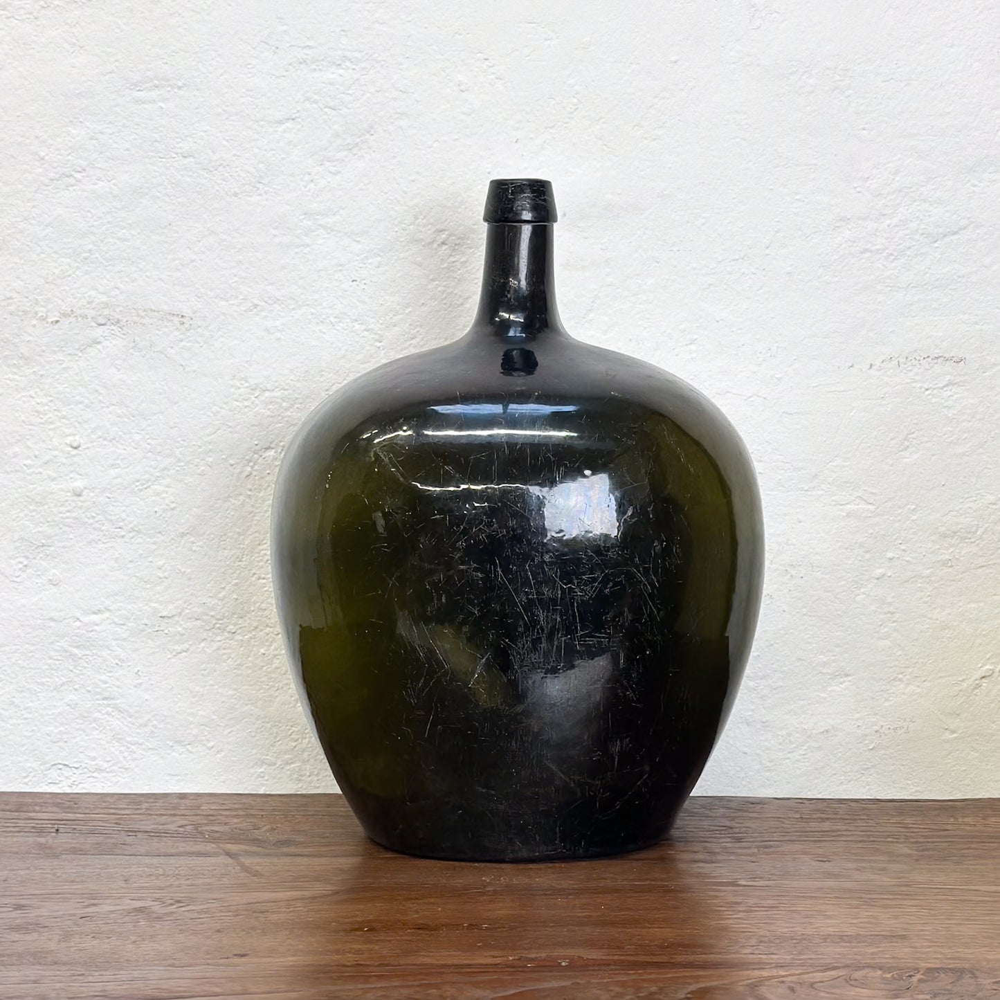 Three oval demijohn glass vases with a dark tint, displayed on a wooden surface against a neutral background.