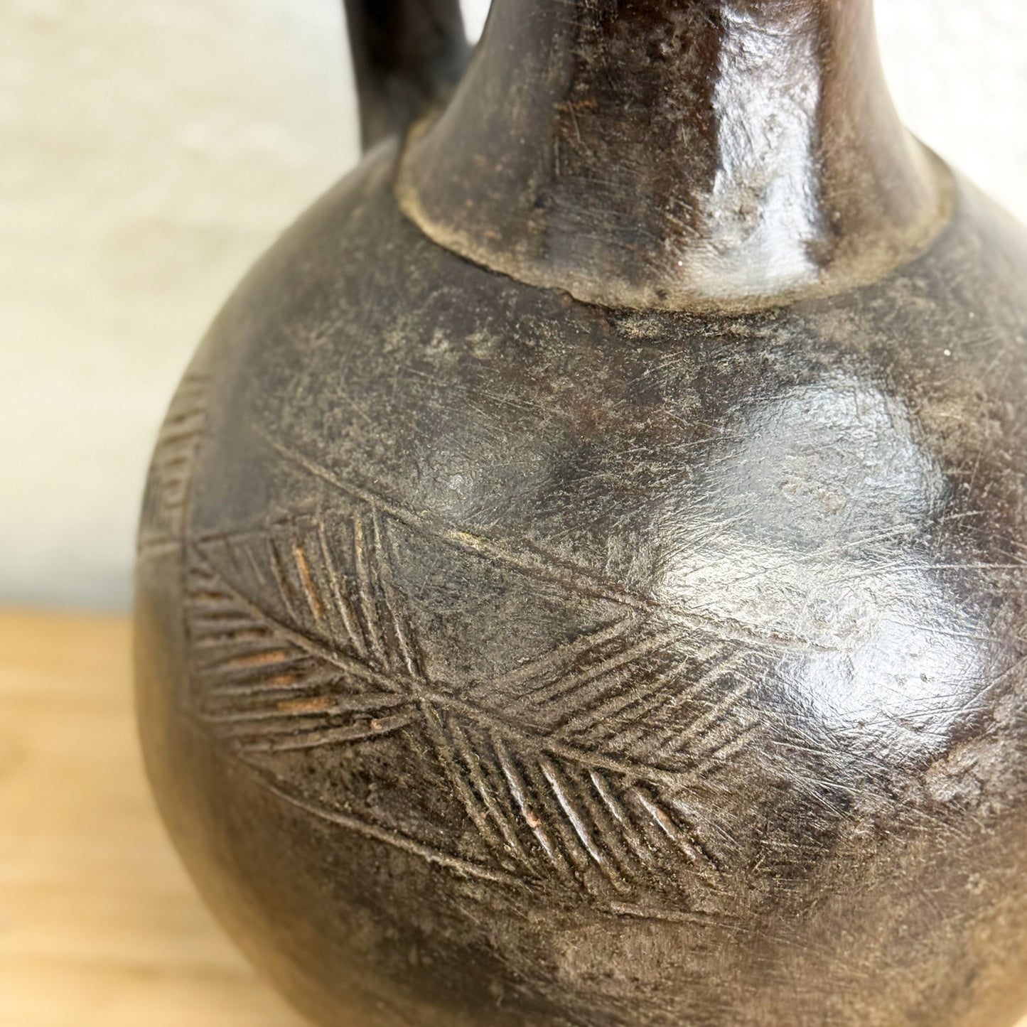 Close-up of a dark brown ceramic vase with engraved patterns on a light background