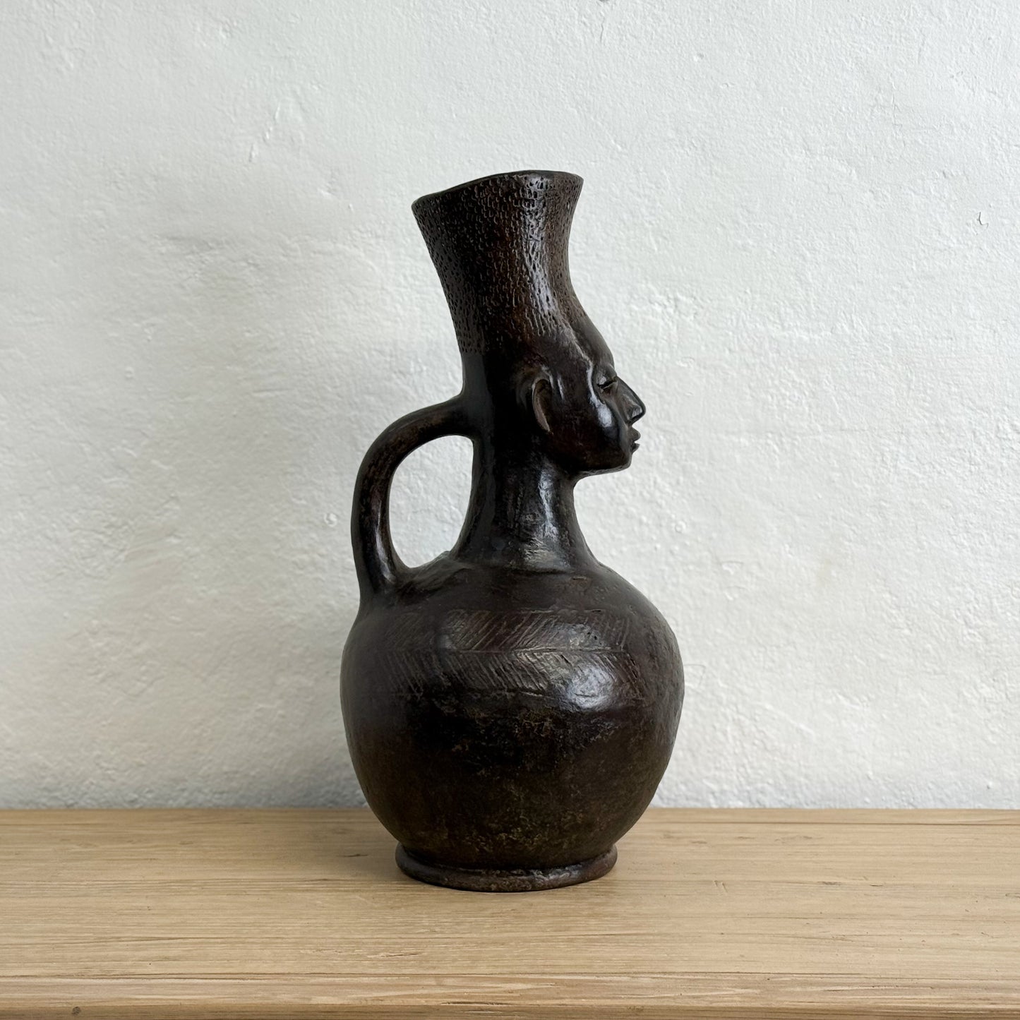 Black ceramic vase with face design on a wooden surface and white wall background