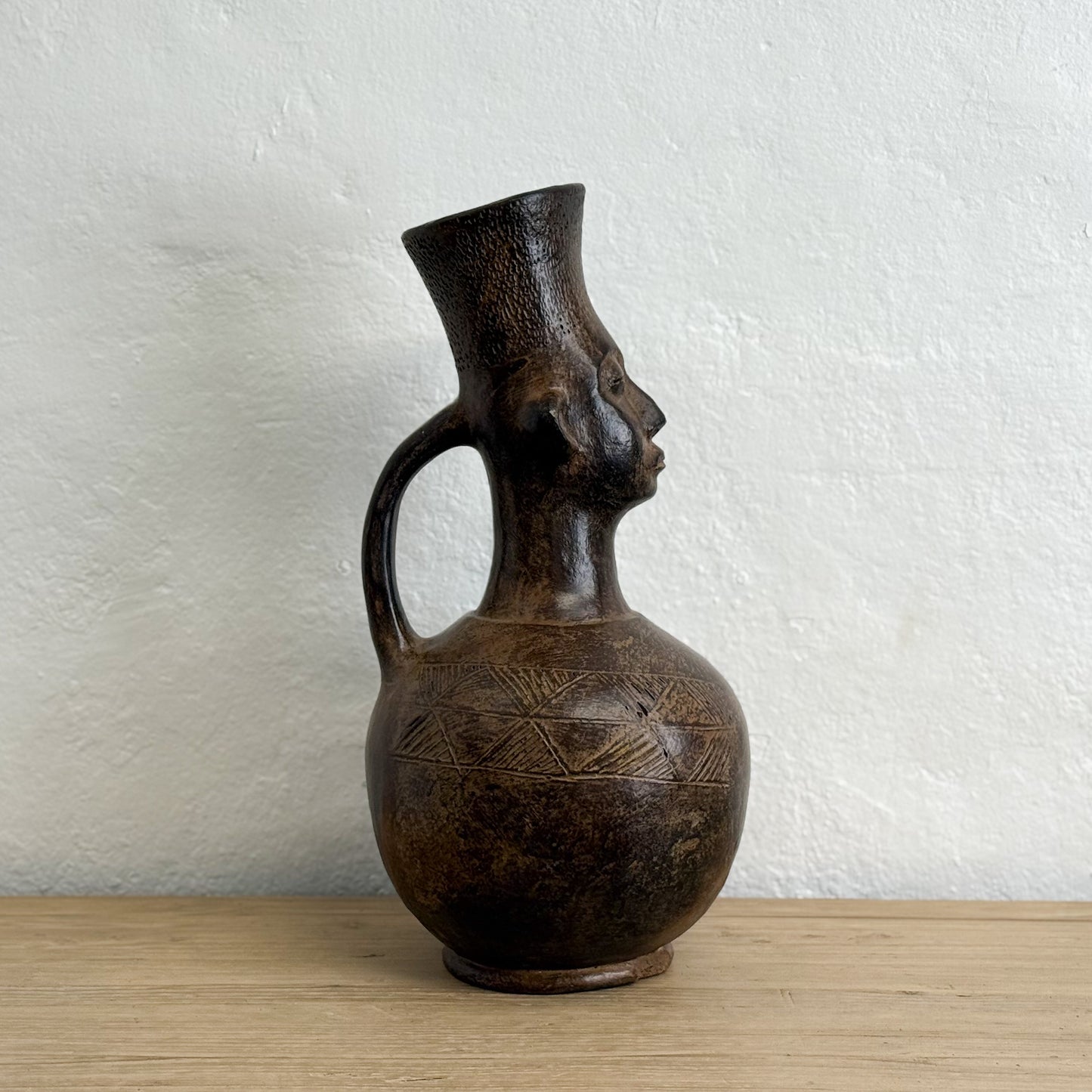 Ceramic vase with face design on a wooden surface and white wall background