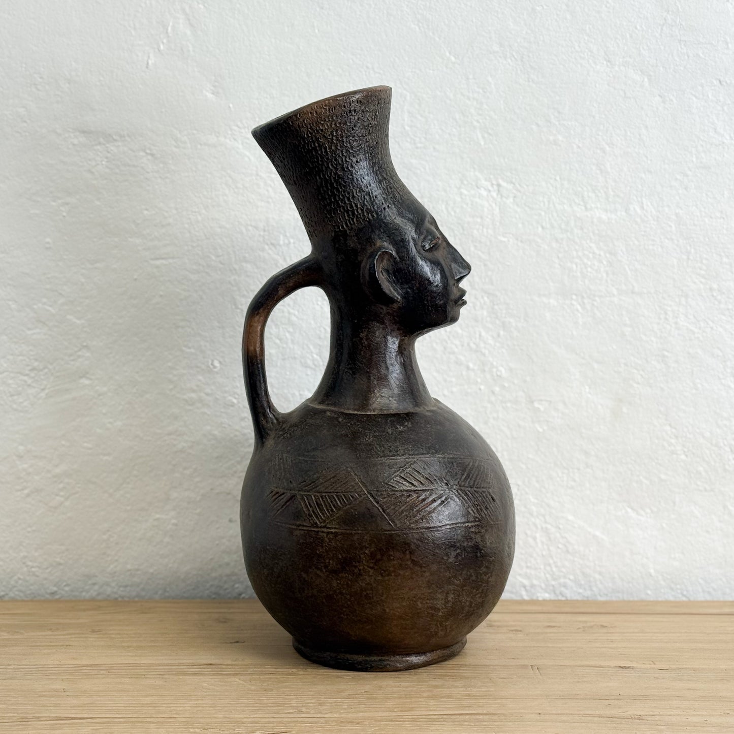 Black ceramic vase with face design on a wooden surface and white wall background