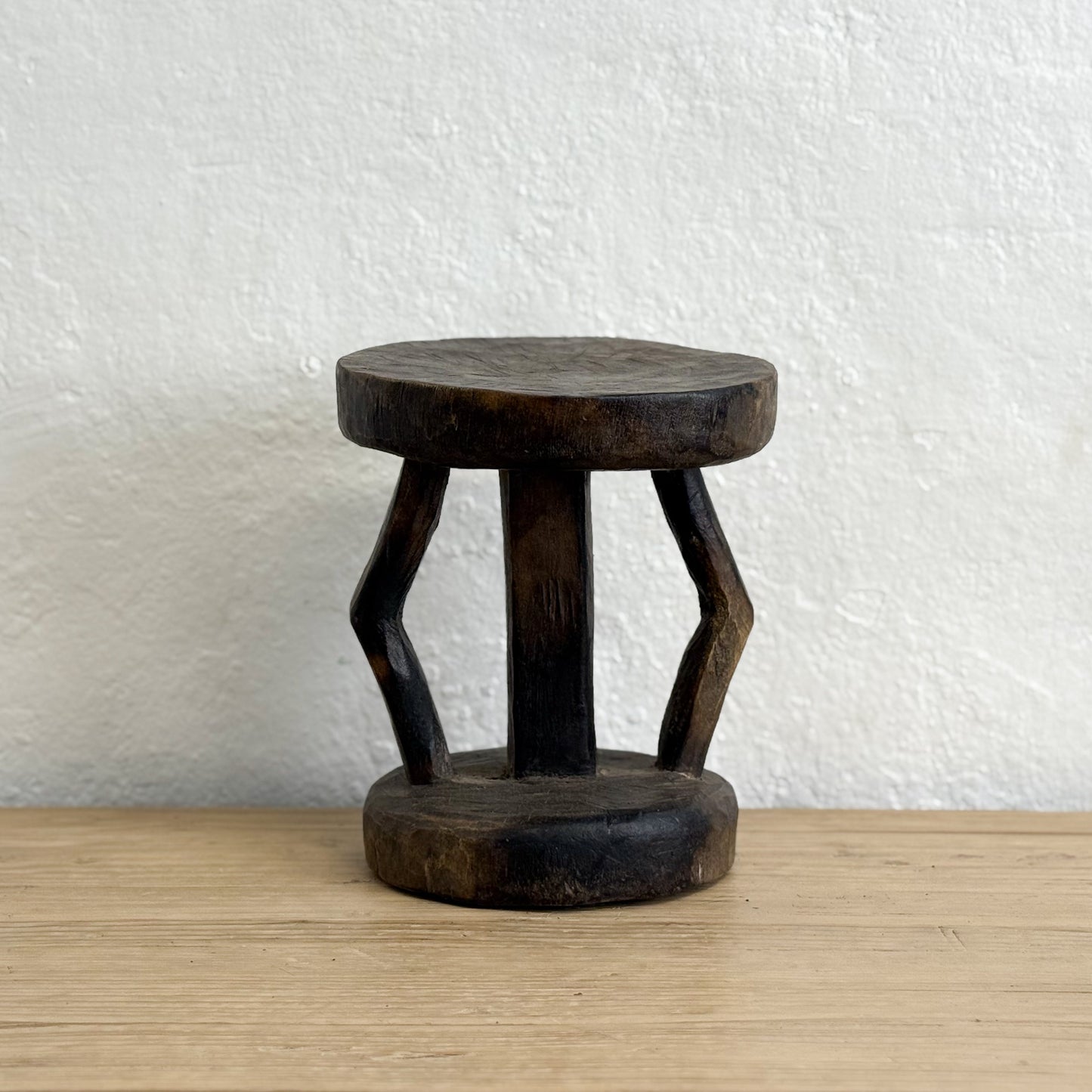Wooden stool with unique design on a wooden surface and white wall background