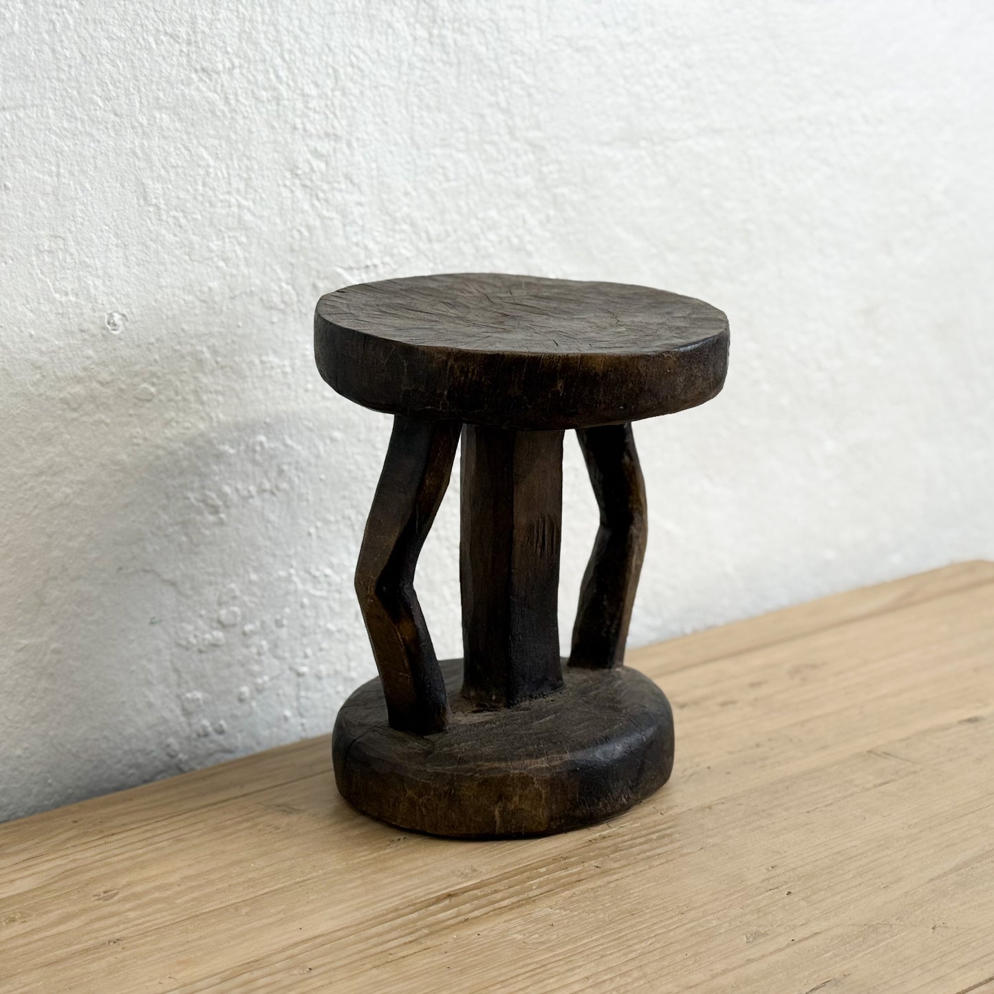 Wooden stool on a wooden surface with a white wall background