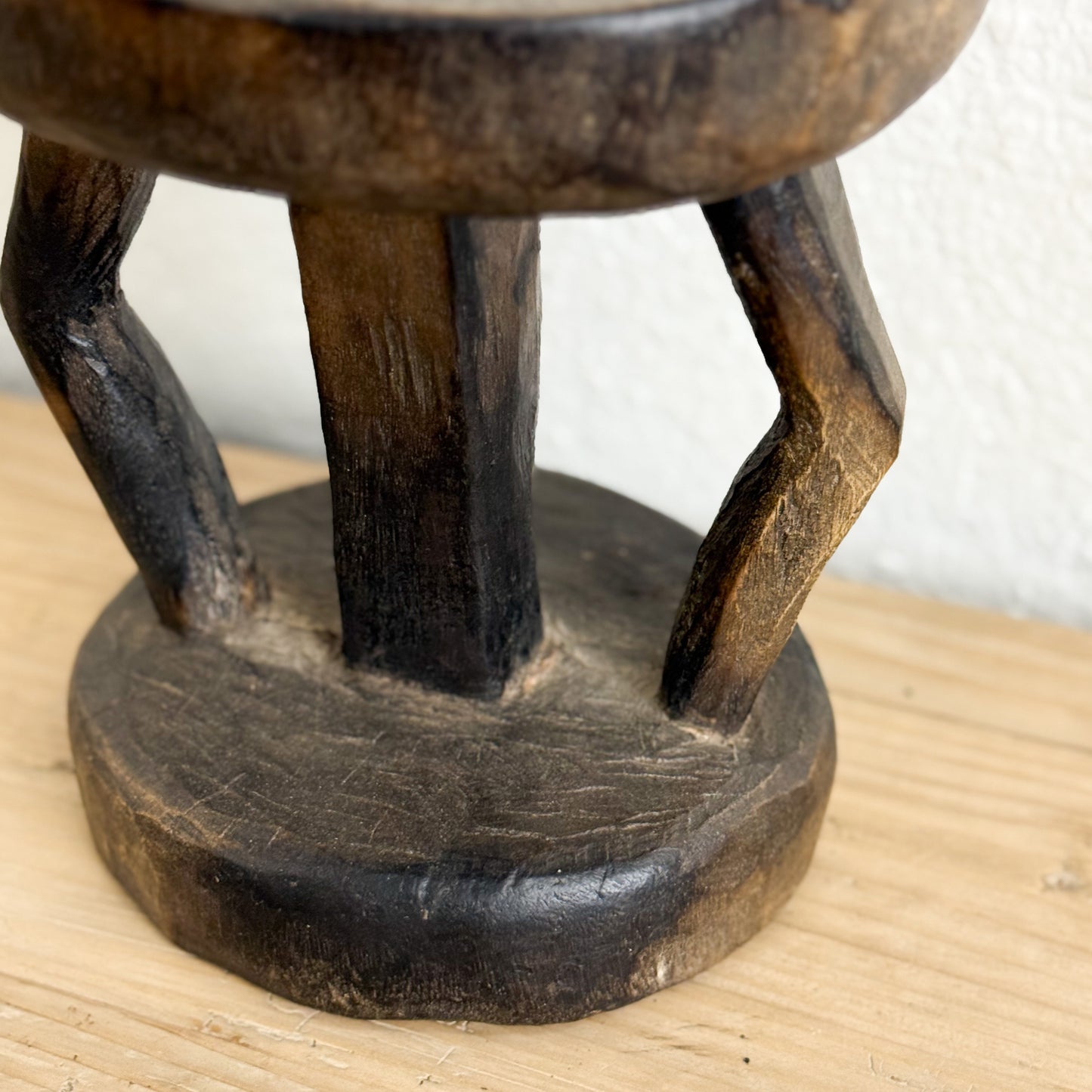 Wooden stool with a round seat and four legs on a wooden surface.