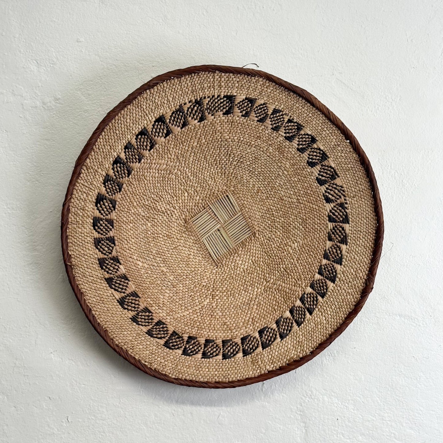 Round woven mat with decorative border on a light gray background