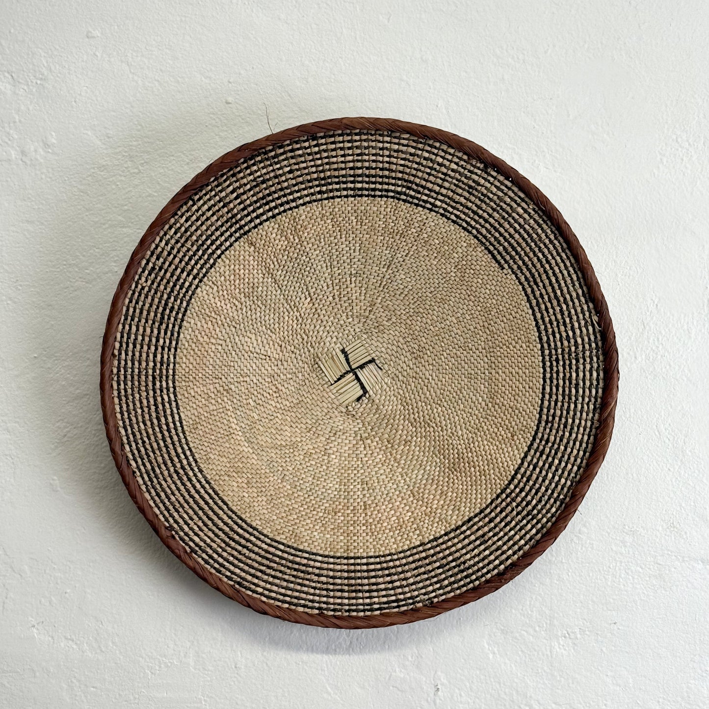 Round woven basket with a central design on a light gray background