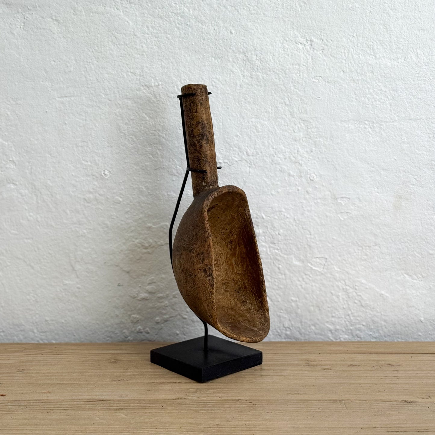 Wooden scoop on a black stand against a white wall