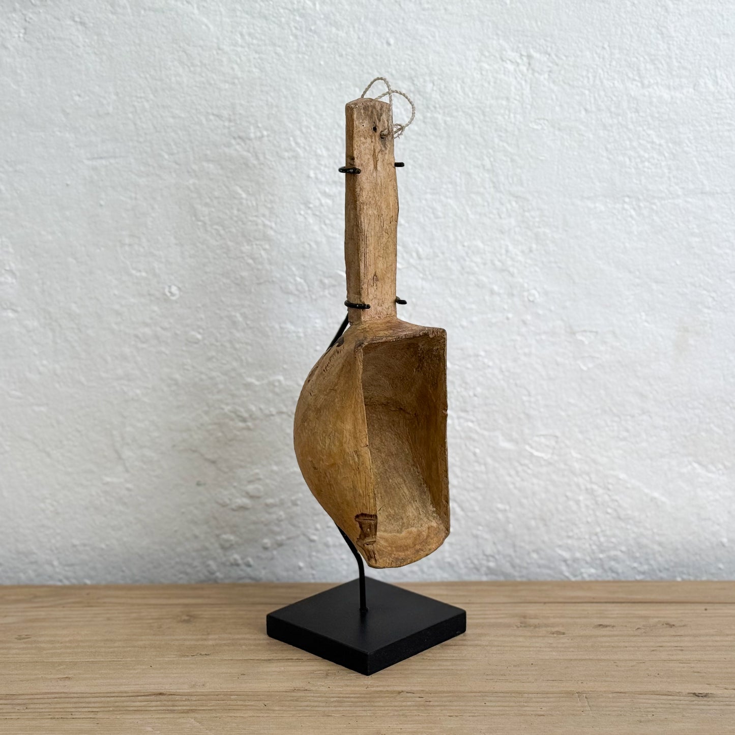 Wooden scoop on a black stand against a white wall
