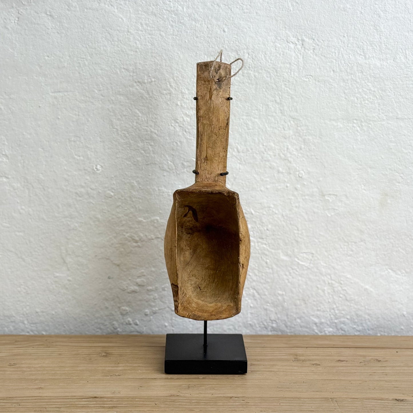 Wooden scoop on a stand against a white wall