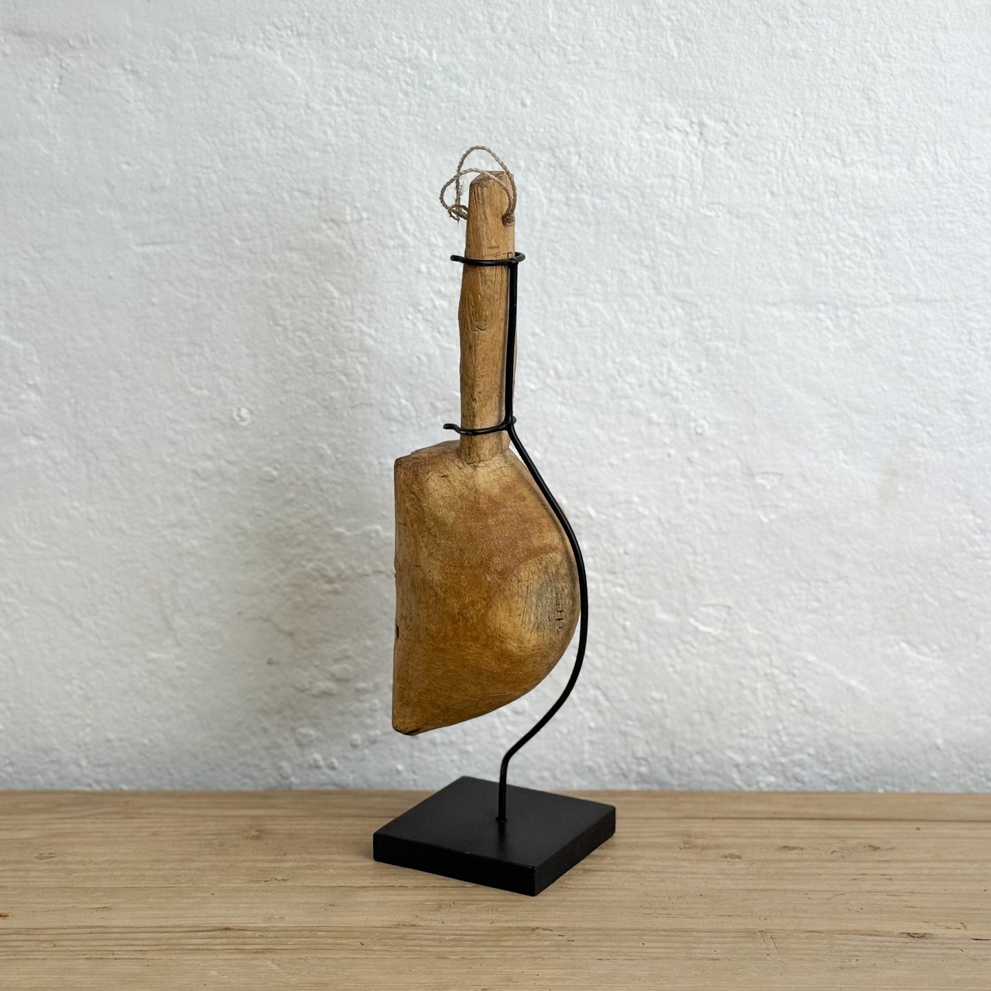 Vintage-style wooden tool on a black stand against a textured white wall.