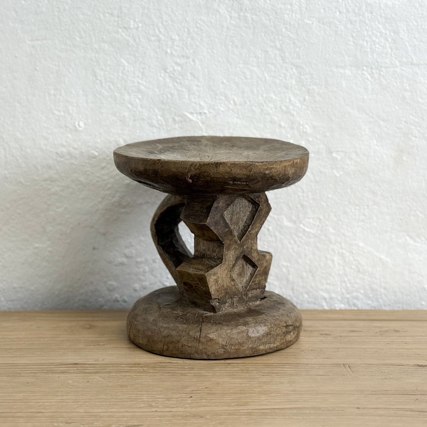 Wooden stool with intricate carvings on a wooden surface and white wall background