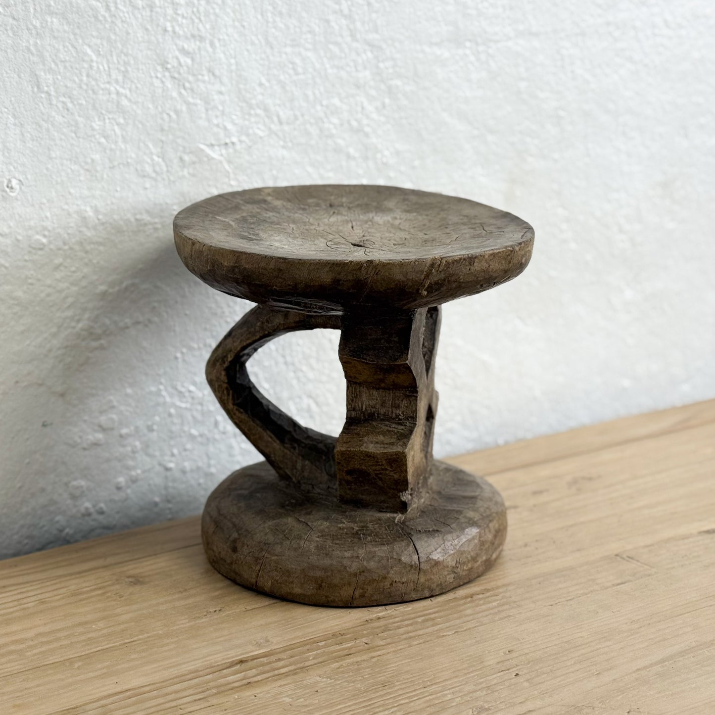 Wooden stool on a wooden surface with a white wall background