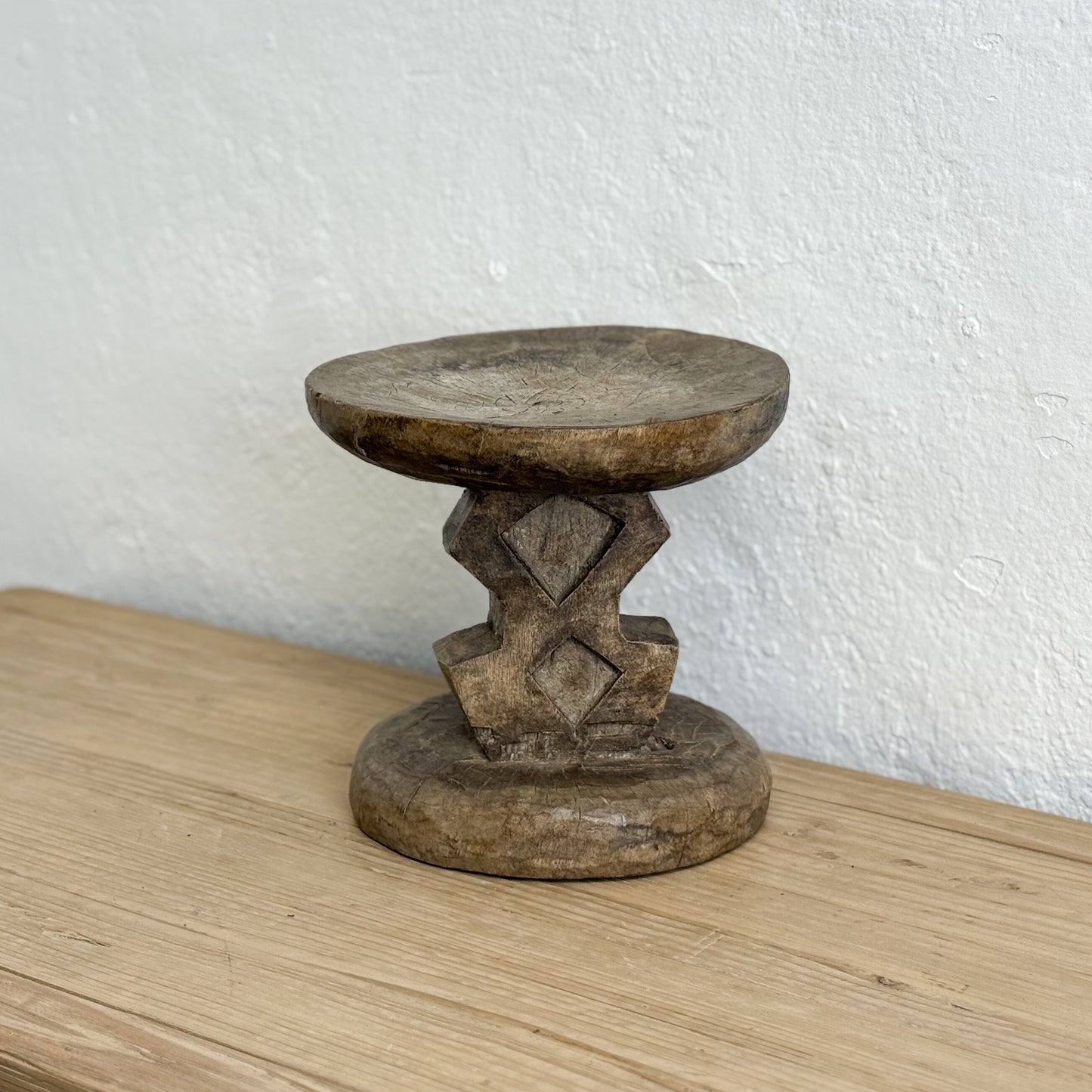 Wooden stool with geometric design on a wooden surface and white wall background