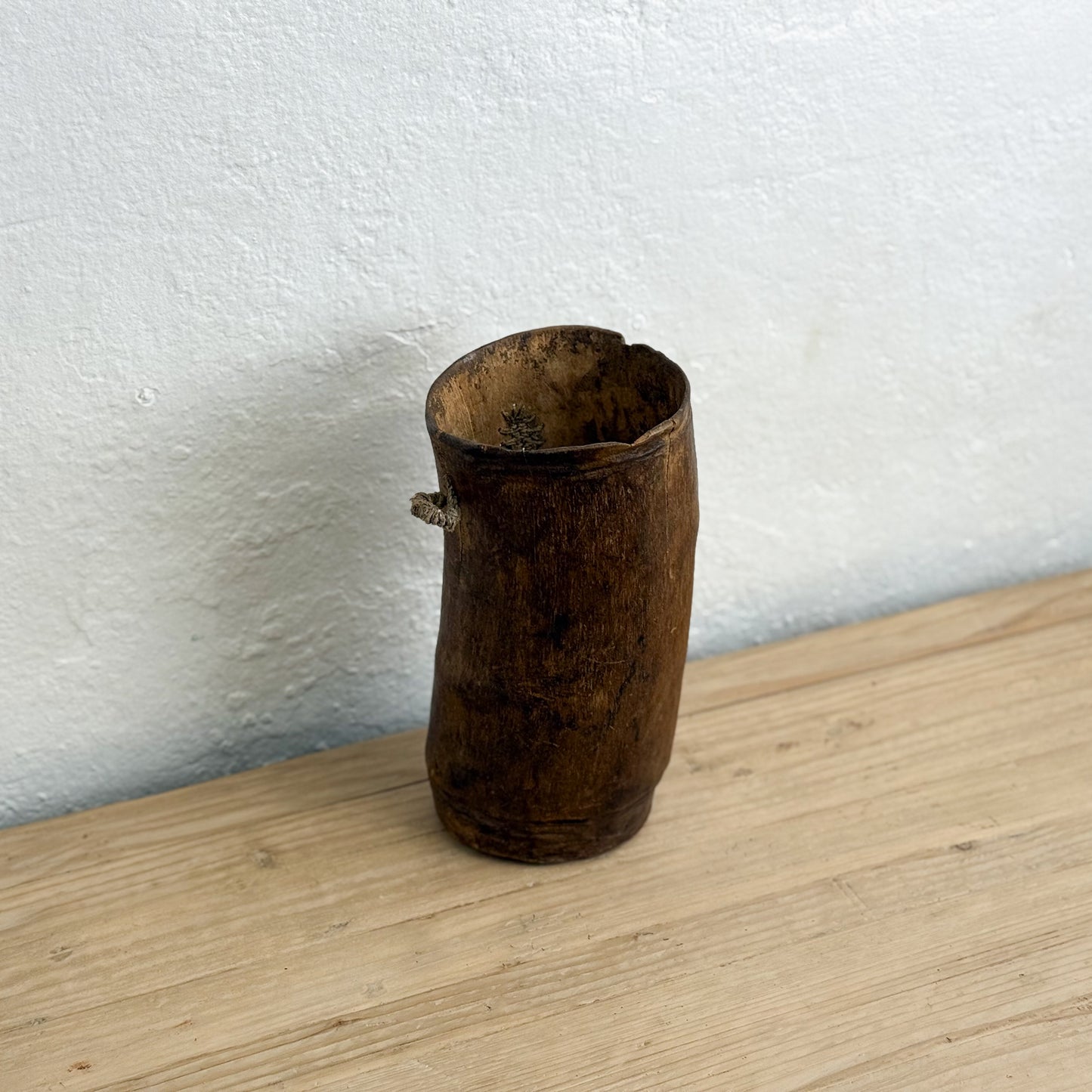 Wooden vase on a wooden surface with a white wall background
