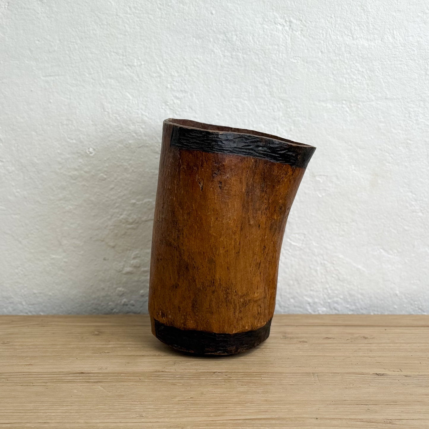 Wooden vase with black base on a wooden surface and white wall background