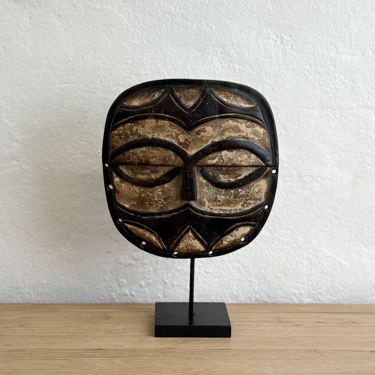 African mask on a stand against a white wall