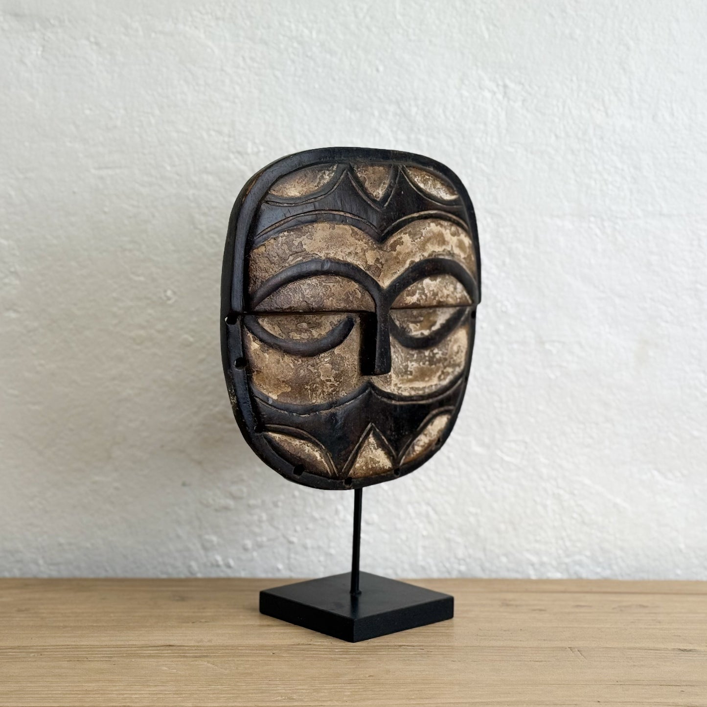 African mask on a stand against a white textured wall.
