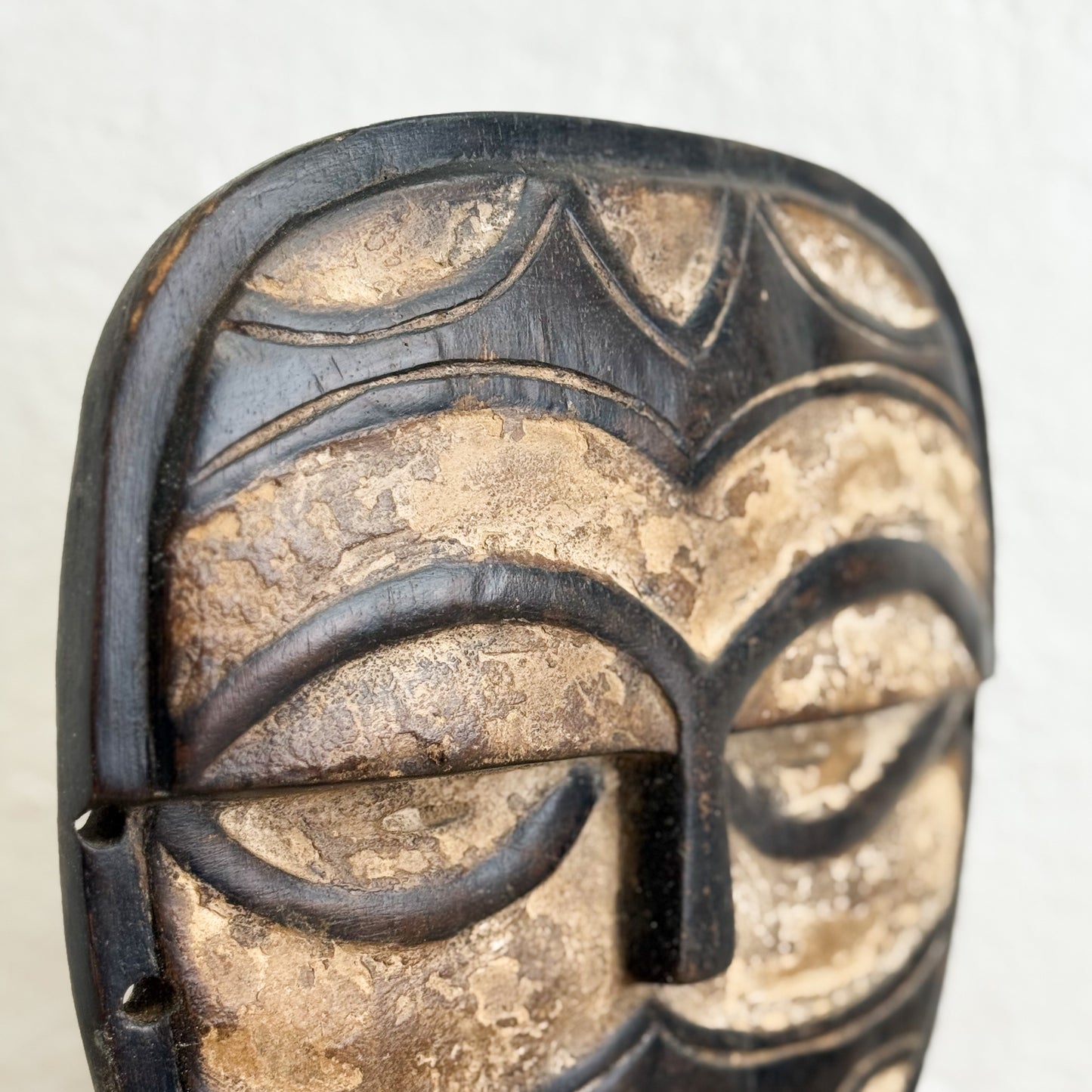 Close-up of a wooden mask with intricate carvings on a white background