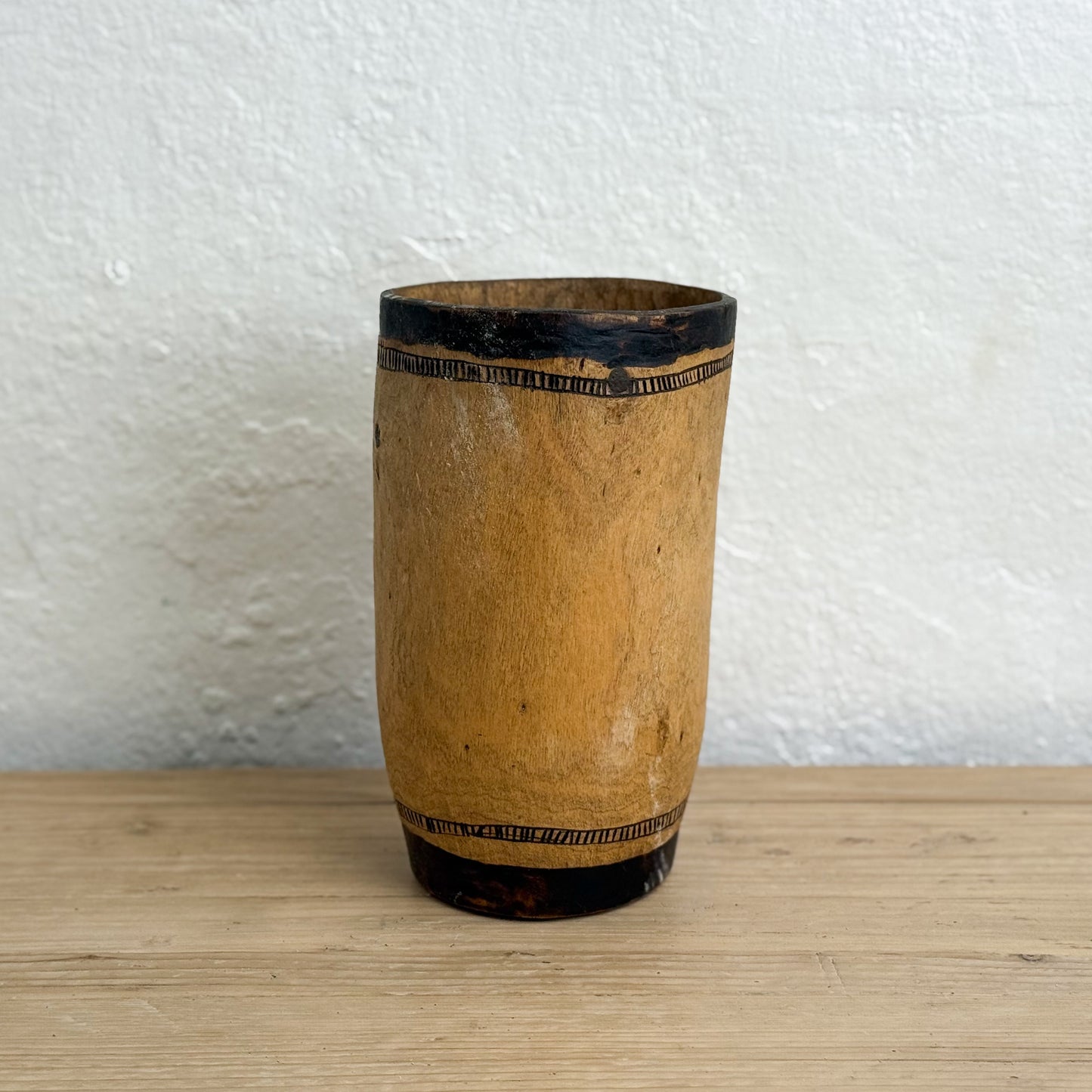 Wooden vase with black banding on a wooden surface and white wall background