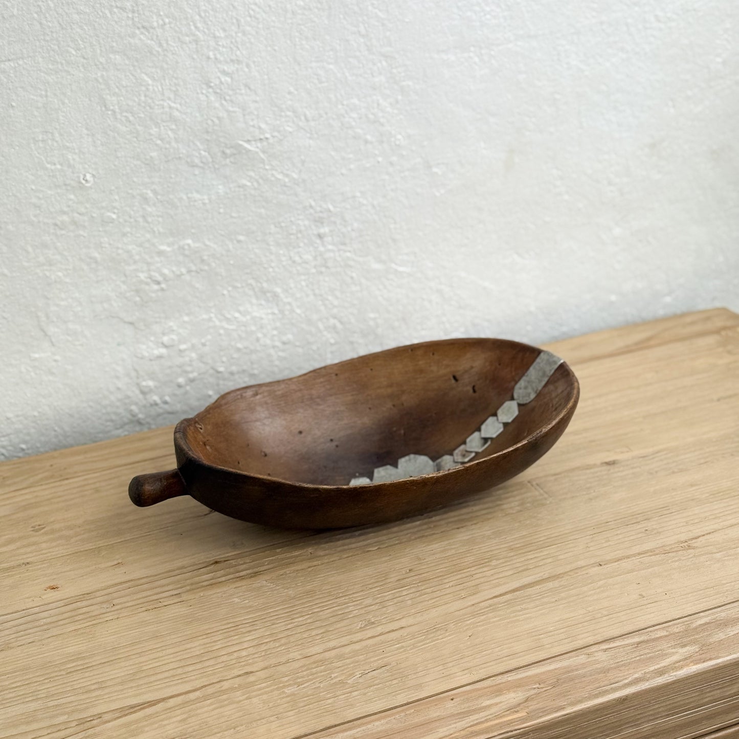 Wooden spoon with a handle on a light wooden surface against a white wall