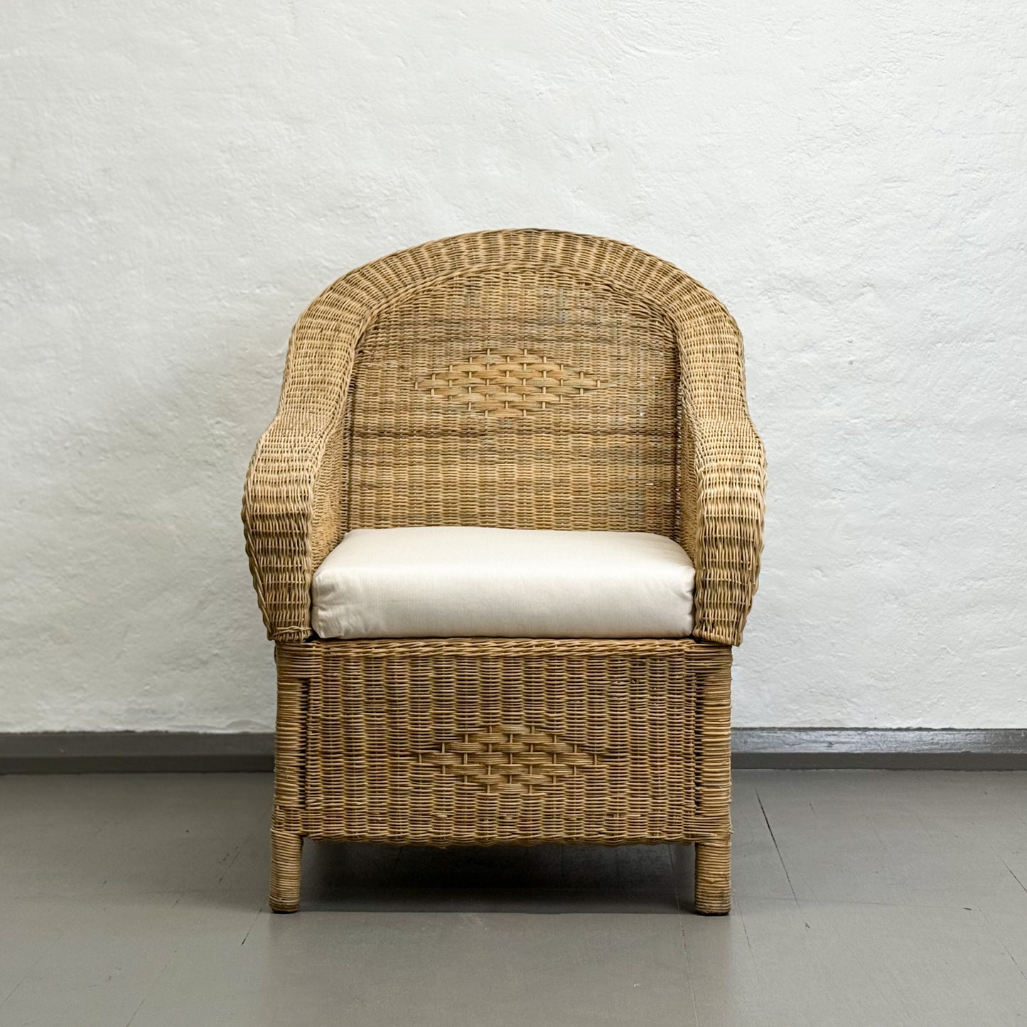 Wicker chair with a white cushion against a light gray wall.