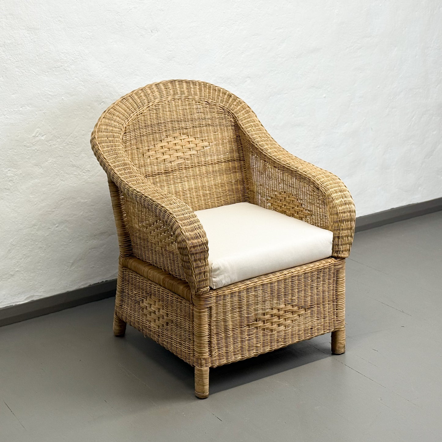 Wicker armchair with a white cushion on a gray floor against a white wall