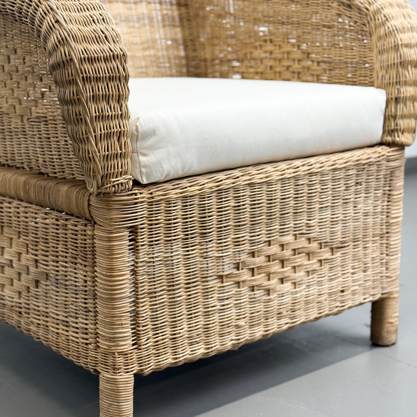 Wicker chair with a white cushion on a gray floor