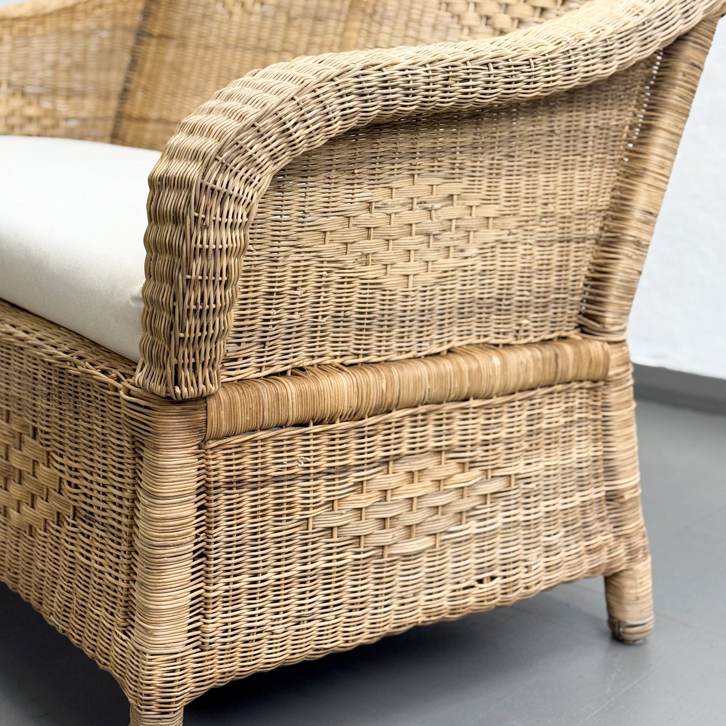 Wicker chair with a white cushion on a gray floor