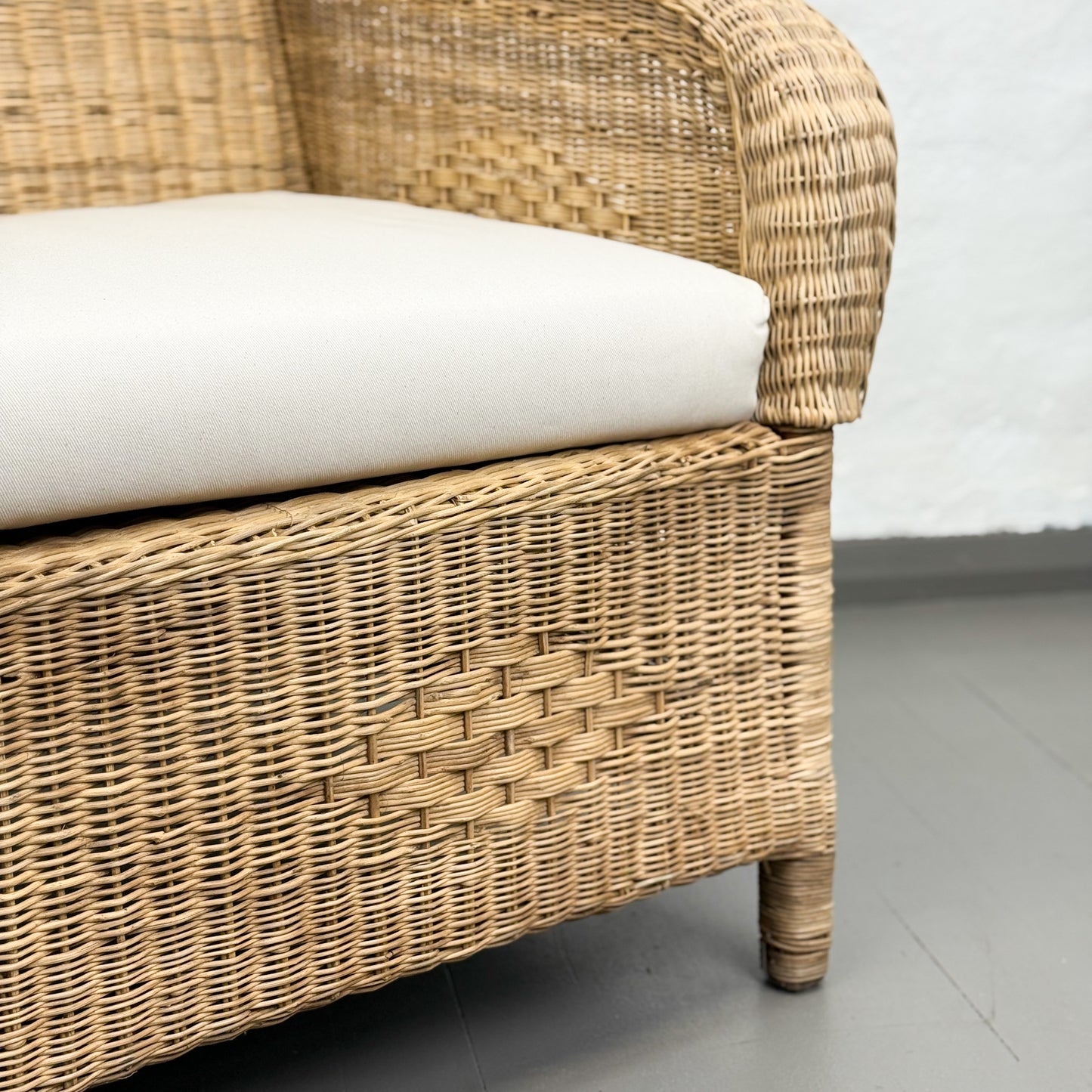 Wicker chair with a white cushion on a gray floor.