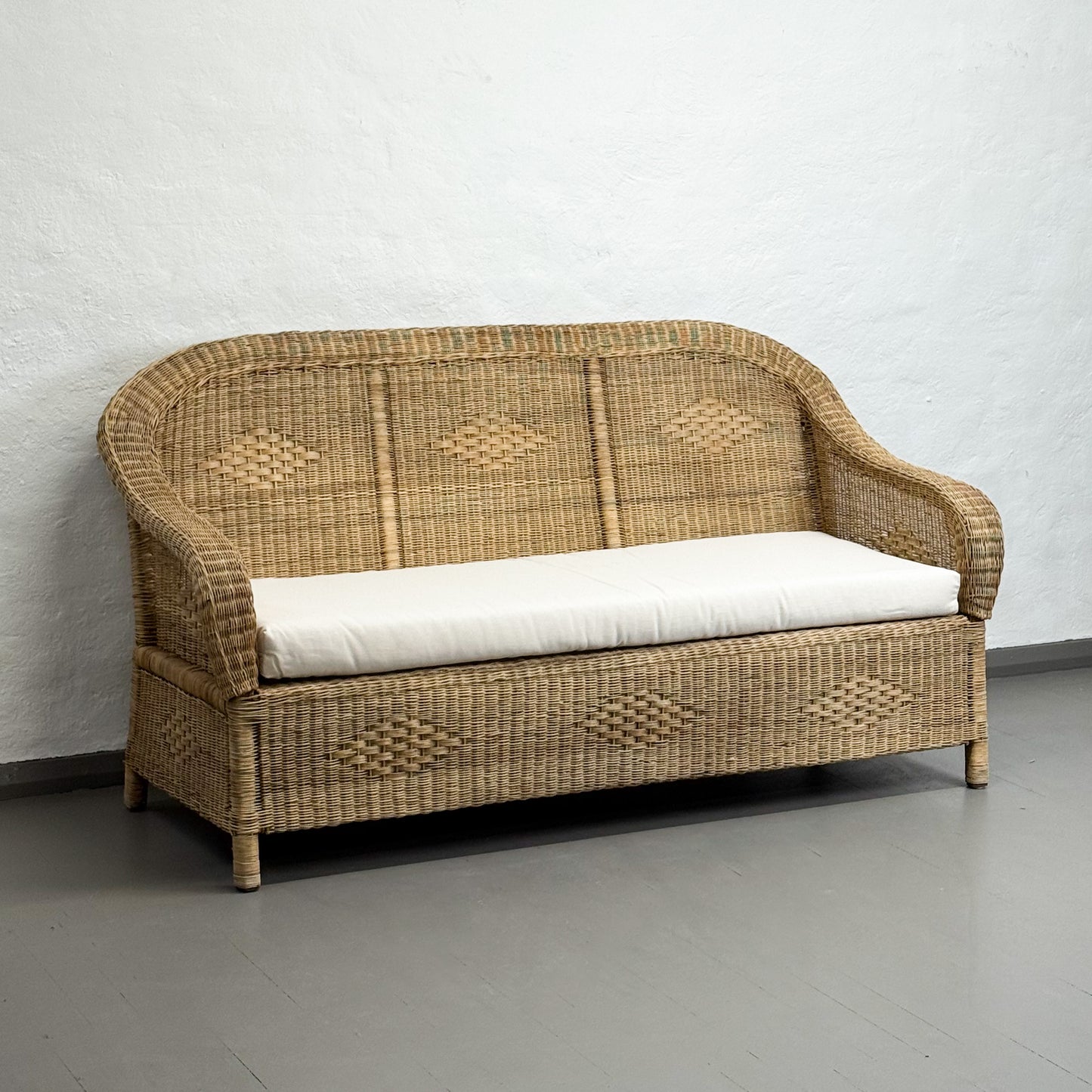 Wicker sofa with a white cushion on a gray floor against a white wall